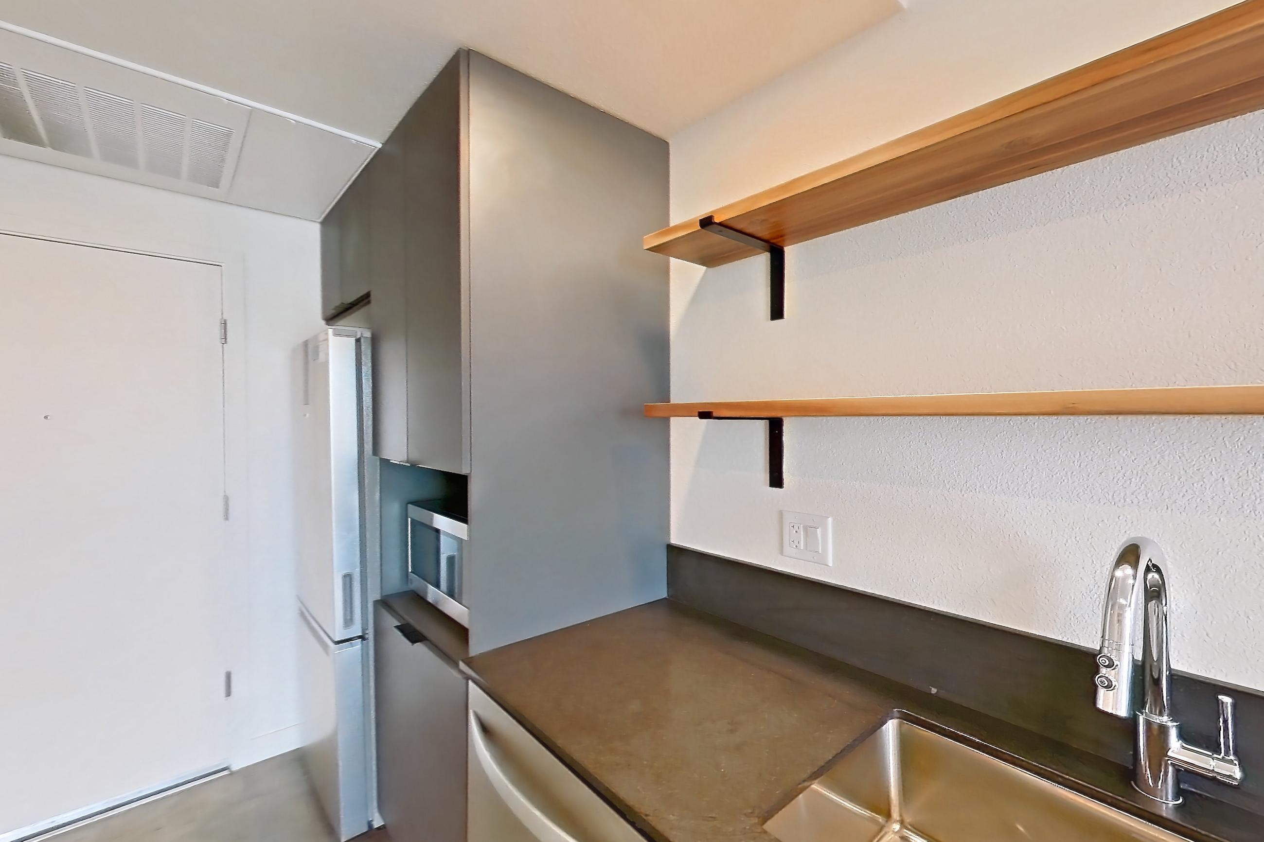 Kitchen with dark countertops, dishwasher, electric range, in-unit laundry, microwave, oven/range, polished concrete flooring, refrigerator, stainless steel appliances, and white appliances, Apartment 2060 at Dwell @ 5th and Farmer