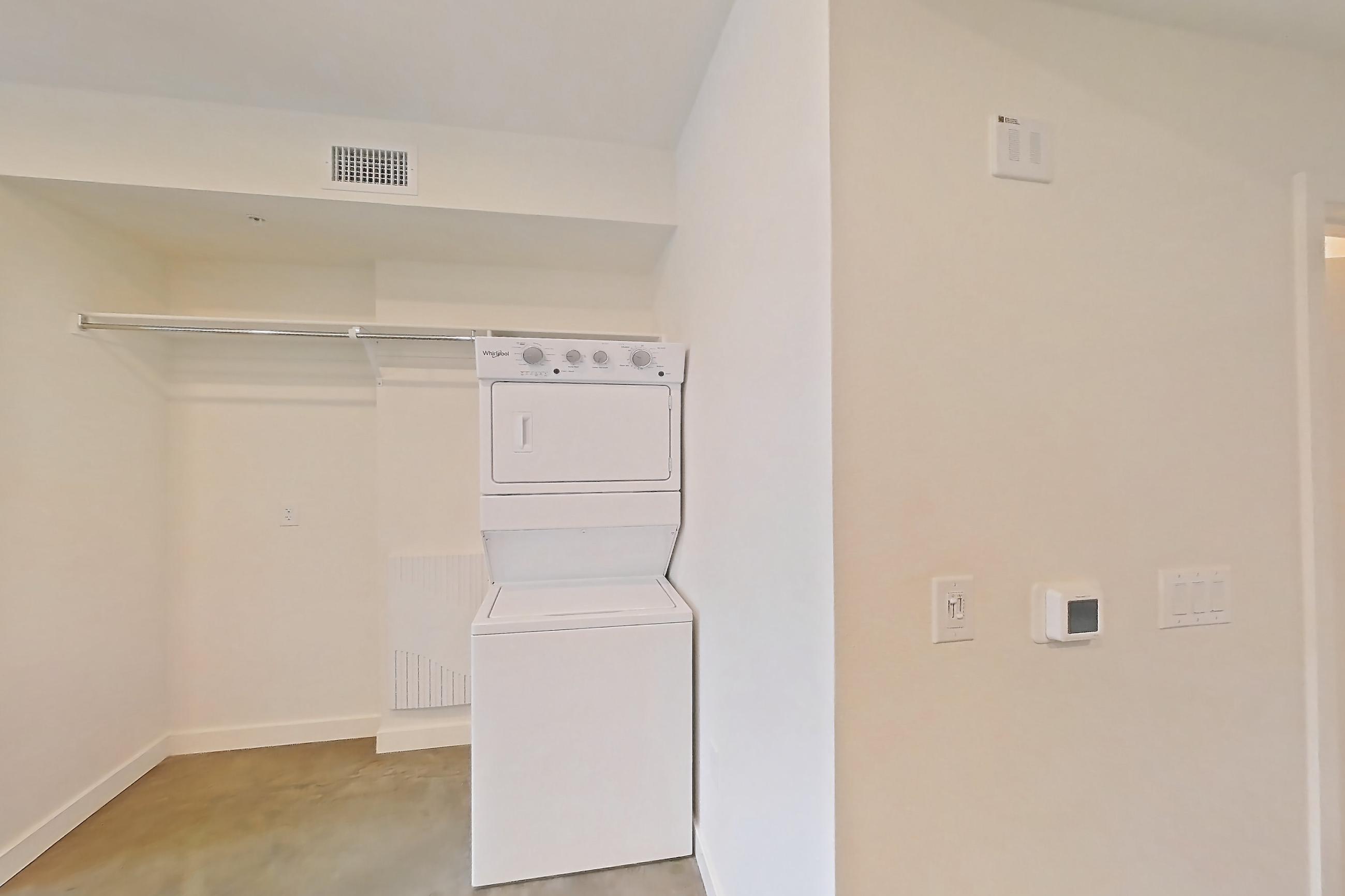 Kitchen with dark countertops, dishwasher, electric range, in-unit laundry, microwave, oven/range, polished concrete flooring, refrigerator, stainless steel appliances, and white appliances, Apartment 2060 at Dwell @ 5th and Farmer