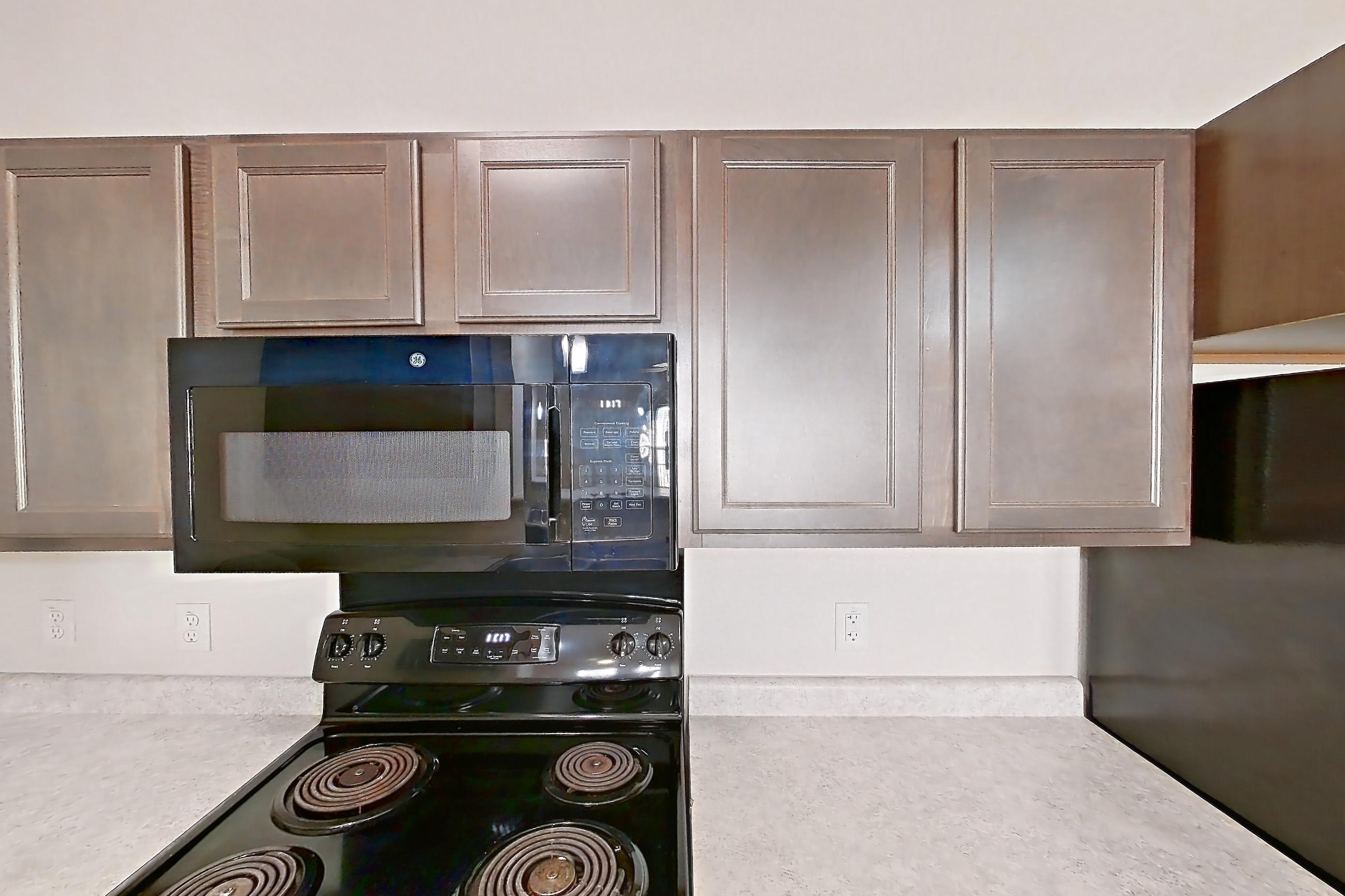 Kitchen with black appliances, electric range, light countertops, light wood-finish flooring, microwave, oven/range, and refrigerator, Apartment 3202 at Residences of Stillwater