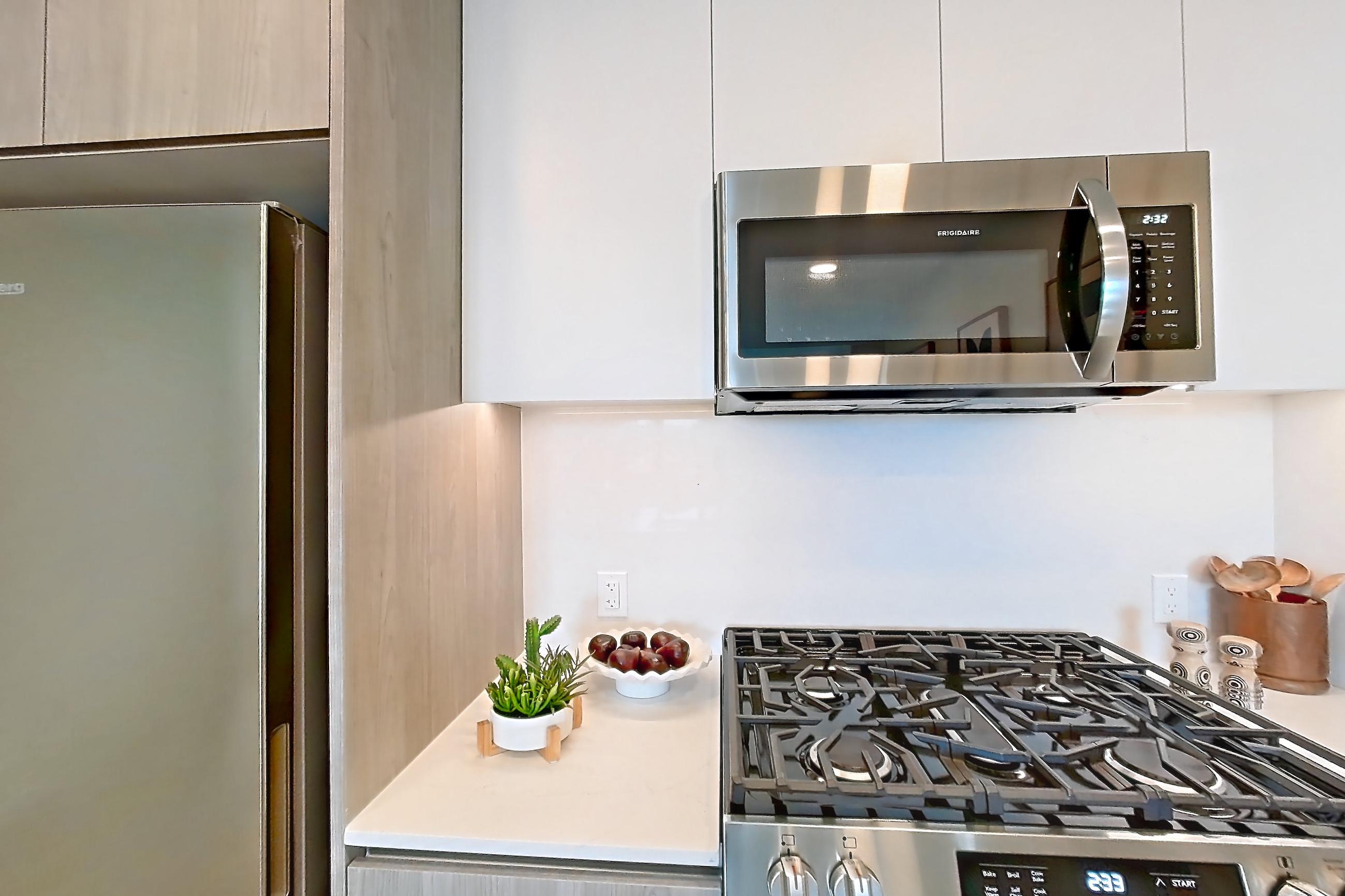 Kitchen with dishwasher, gas range, light countertops, light stone countertops, light wood-finish flooring, microwave, oven/range, refrigerator, and stainless steel appliances, Apartment 924 at Loden