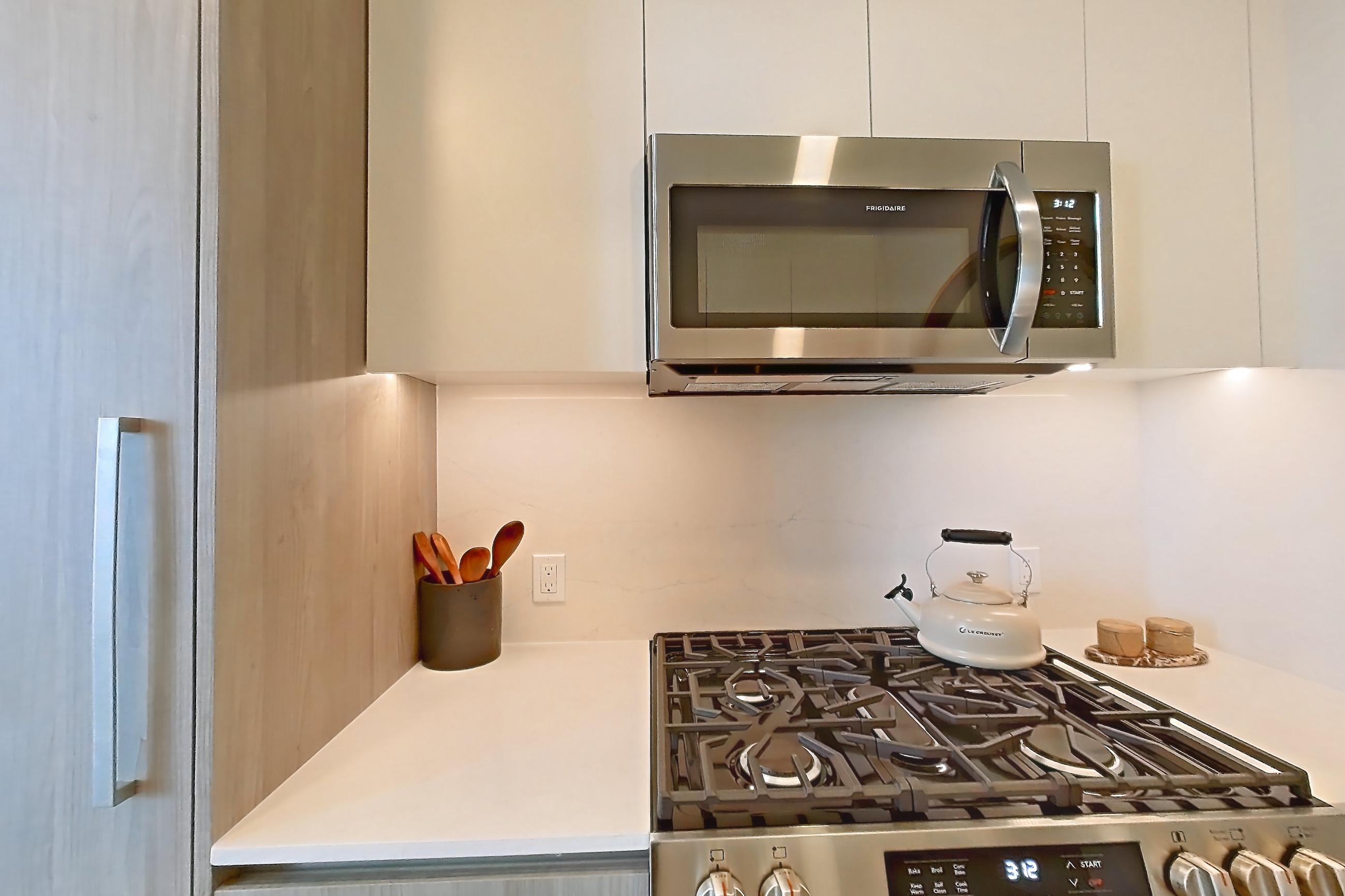 Kitchen with gas range, light countertops, light stone countertops, light wood-finish flooring, microwave, oven/range, and stainless steel appliances, Apartment PH16 at Loden