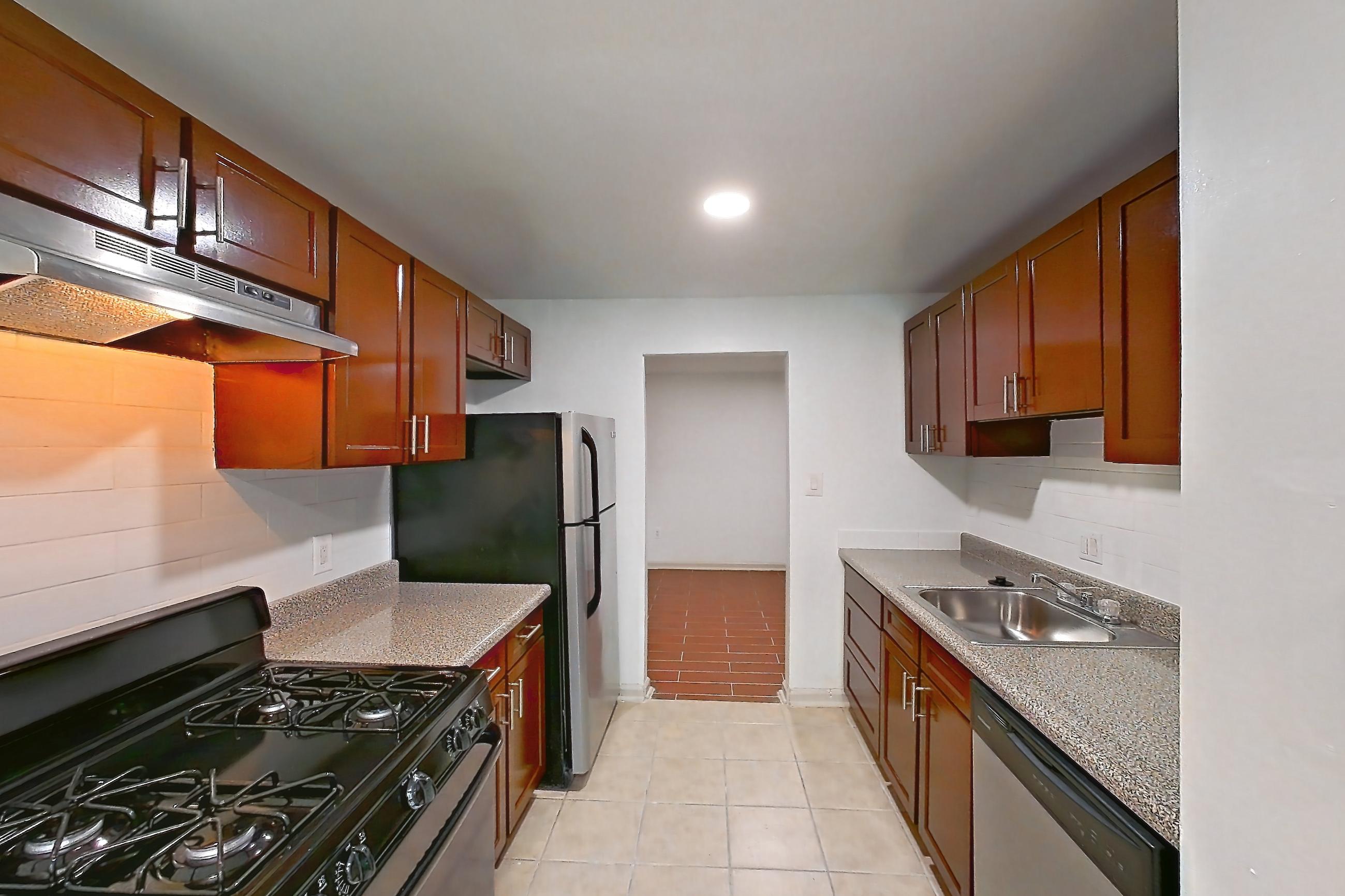 Kitchen with black appliances, dishwasher, gas range, light countertops, light tile flooring, oven/range, range hood, refrigerator, and stainless steel appliances, Apartment 9318ER14 at Franklin Park at Greenbelt Station