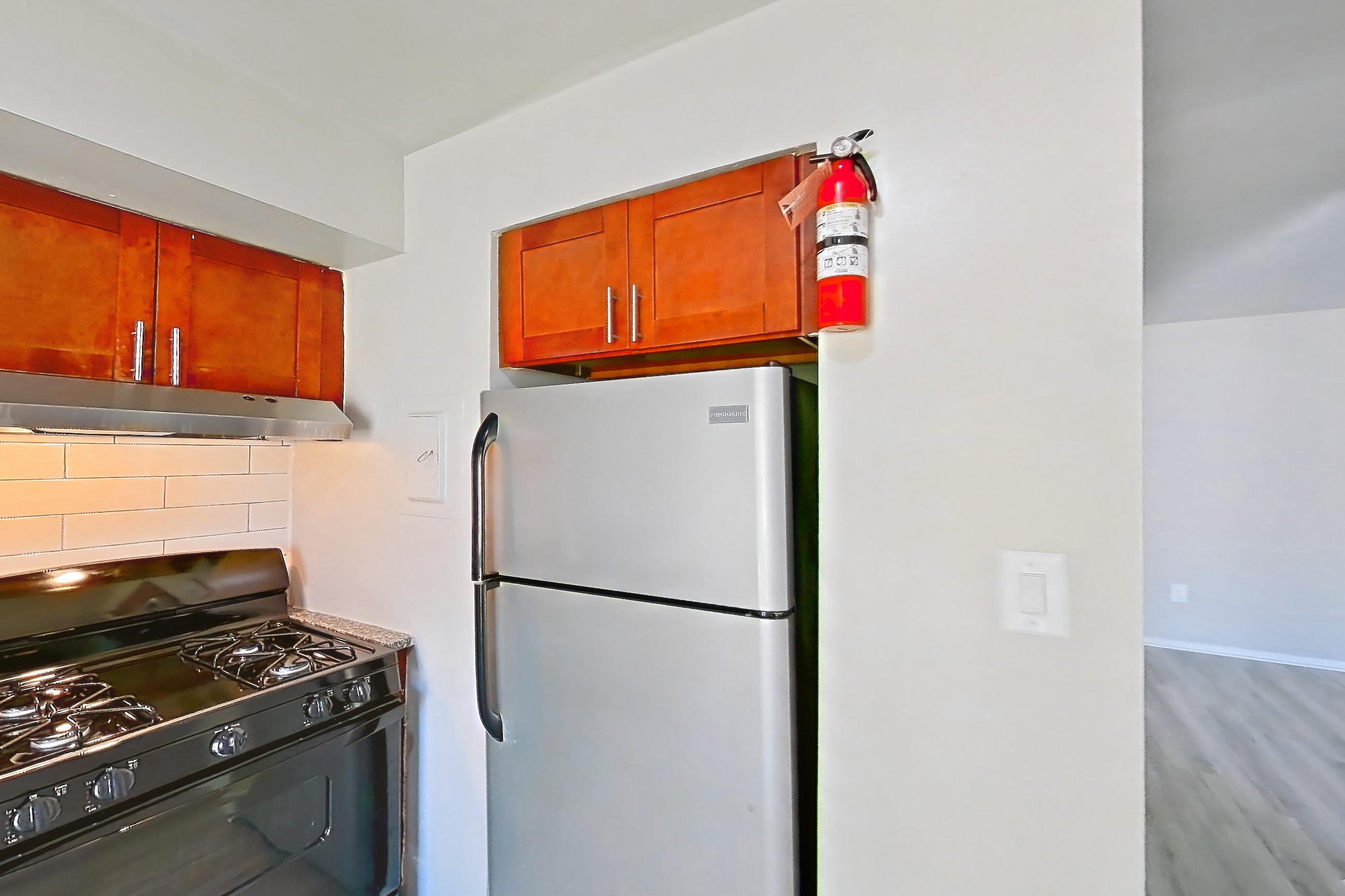 Kitchen with black appliances, dark stone countertops, dishwasher, gas range, light wood-finish flooring, oven/range, range hood, refrigerator, and stainless steel appliances, Apartment 5807CL31 at Franklin Park at Greenbelt Station