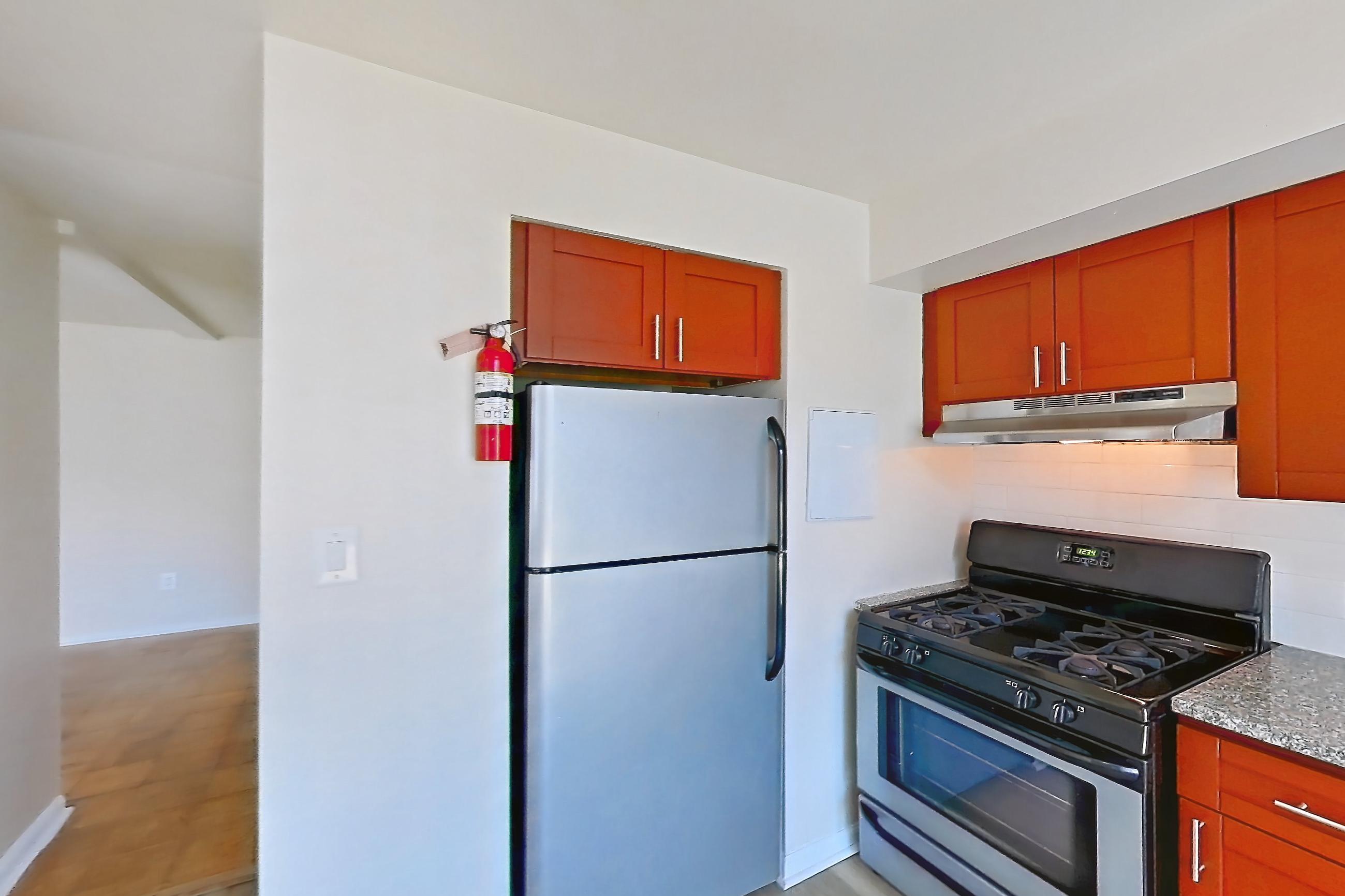 Kitchen with dishwasher, gas range, light countertops, light stone countertops, light wood-finish flooring, oven/range, range hood, refrigerator, stainless steel appliances, and white appliances, Apartment 5809CT24 at Franklin Park at Greenbelt Station