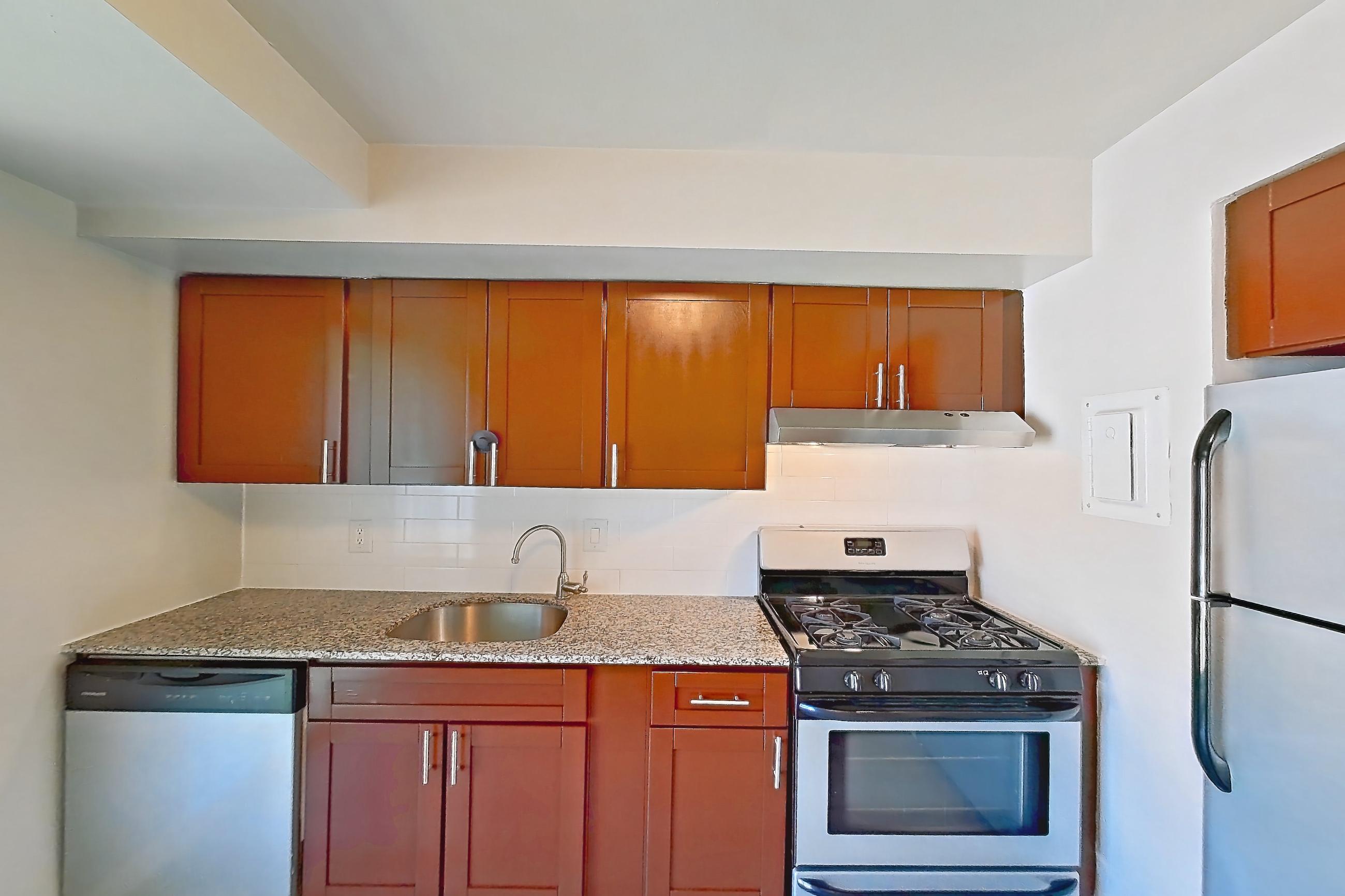 Kitchen with dishwasher, electric range, gas range, light countertops, light stone countertops, light wood-finish flooring, oven/range, refrigerator, and stainless steel appliances, Apartment 5811CL31 at Franklin Park at Greenbelt Station