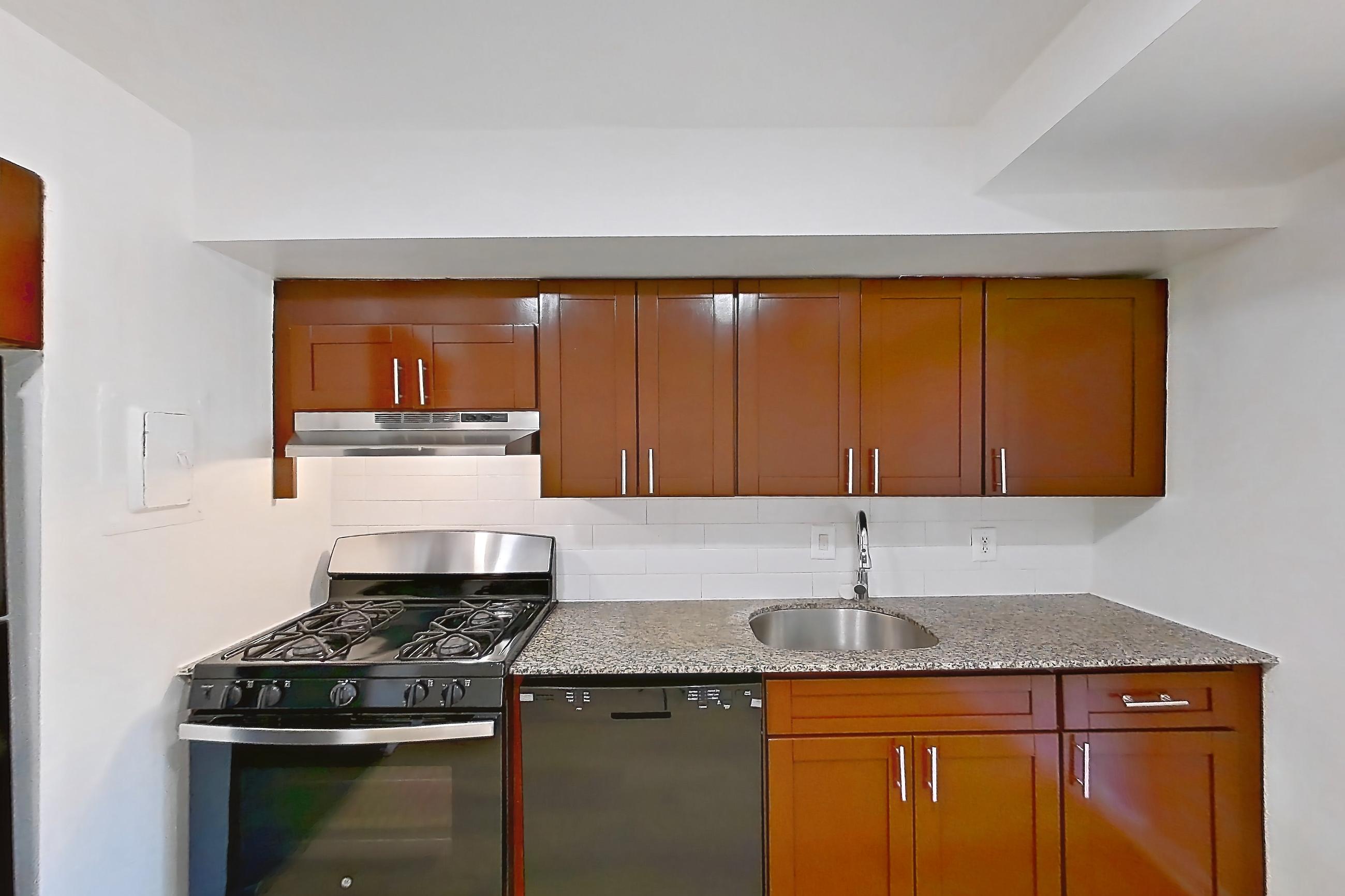 Kitchen with black appliances, dark stone countertops, dishwasher, gas range, light countertops, light wood-finish flooring, oven/range, refrigerator, and stainless steel appliances, Apartment 5811CL34 at Franklin Park at Greenbelt Station