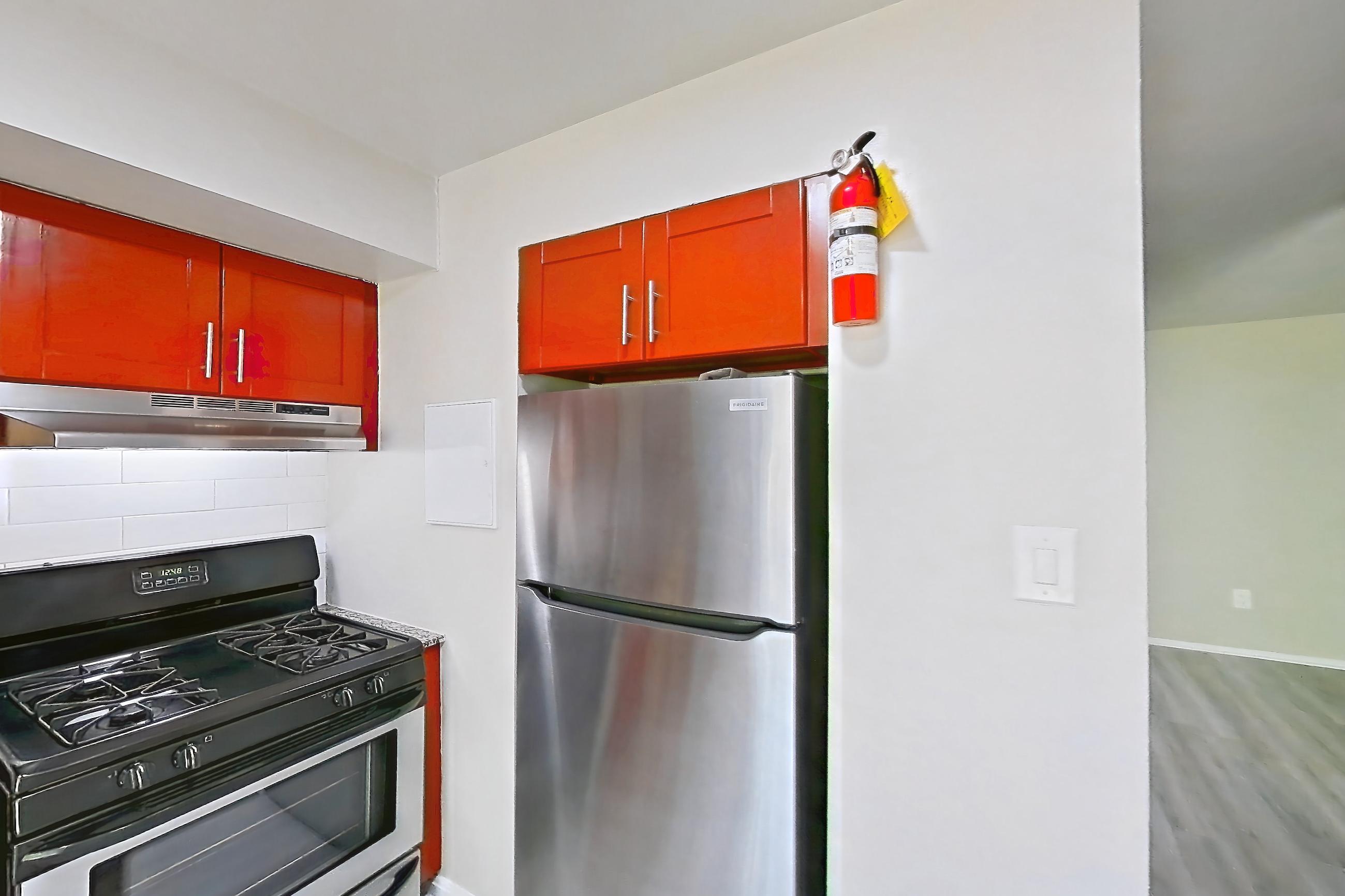 Kitchen with dishwasher, gas range, light countertops, light stone countertops, light wood-finish flooring, oven/range, range hood, refrigerator, and stainless steel appliances, Apartment 5811CT33 at Franklin Park at Greenbelt Station