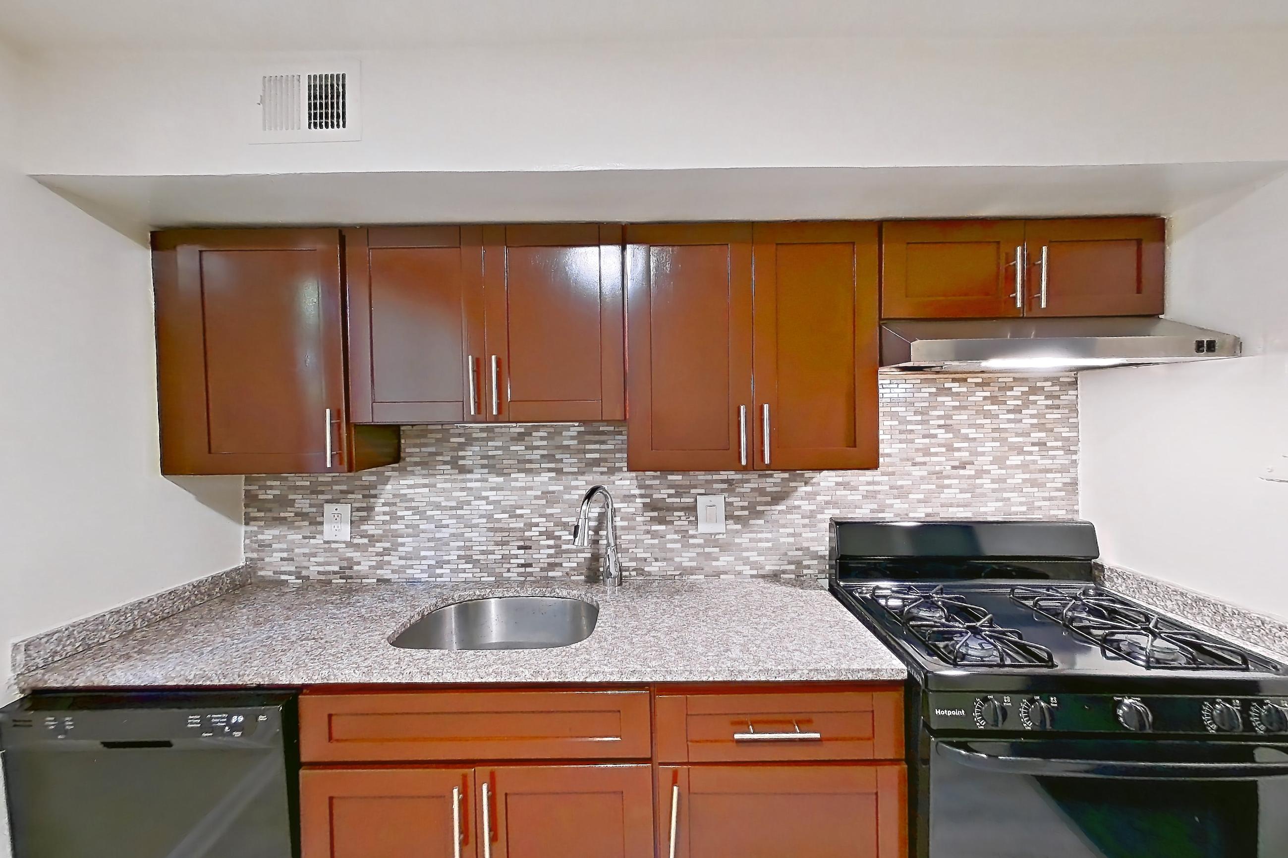 Kitchen with black appliances, dishwasher, gas range, light countertops, light stone countertops, light wood-finish flooring, oven/range, and refrigerator, Apartment 5819CL11 at Franklin Park at Greenbelt Station