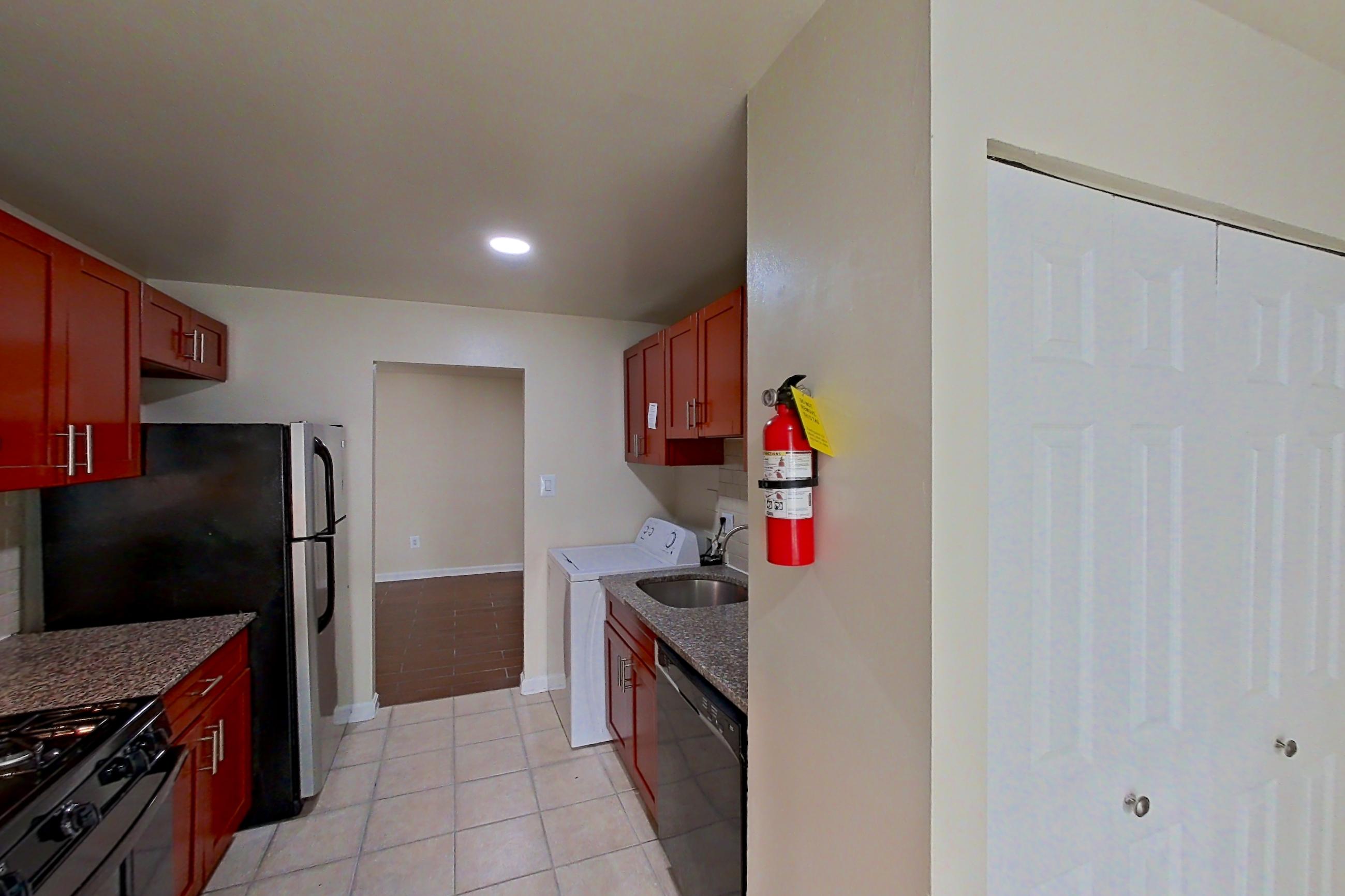 Kitchen with black appliances, dark stone countertops, dishwasher, gas range, in-unit laundry, light countertops, light tile flooring, oven/range, and range hood, Apartment 9326ER12 at Franklin Park at Greenbelt Station