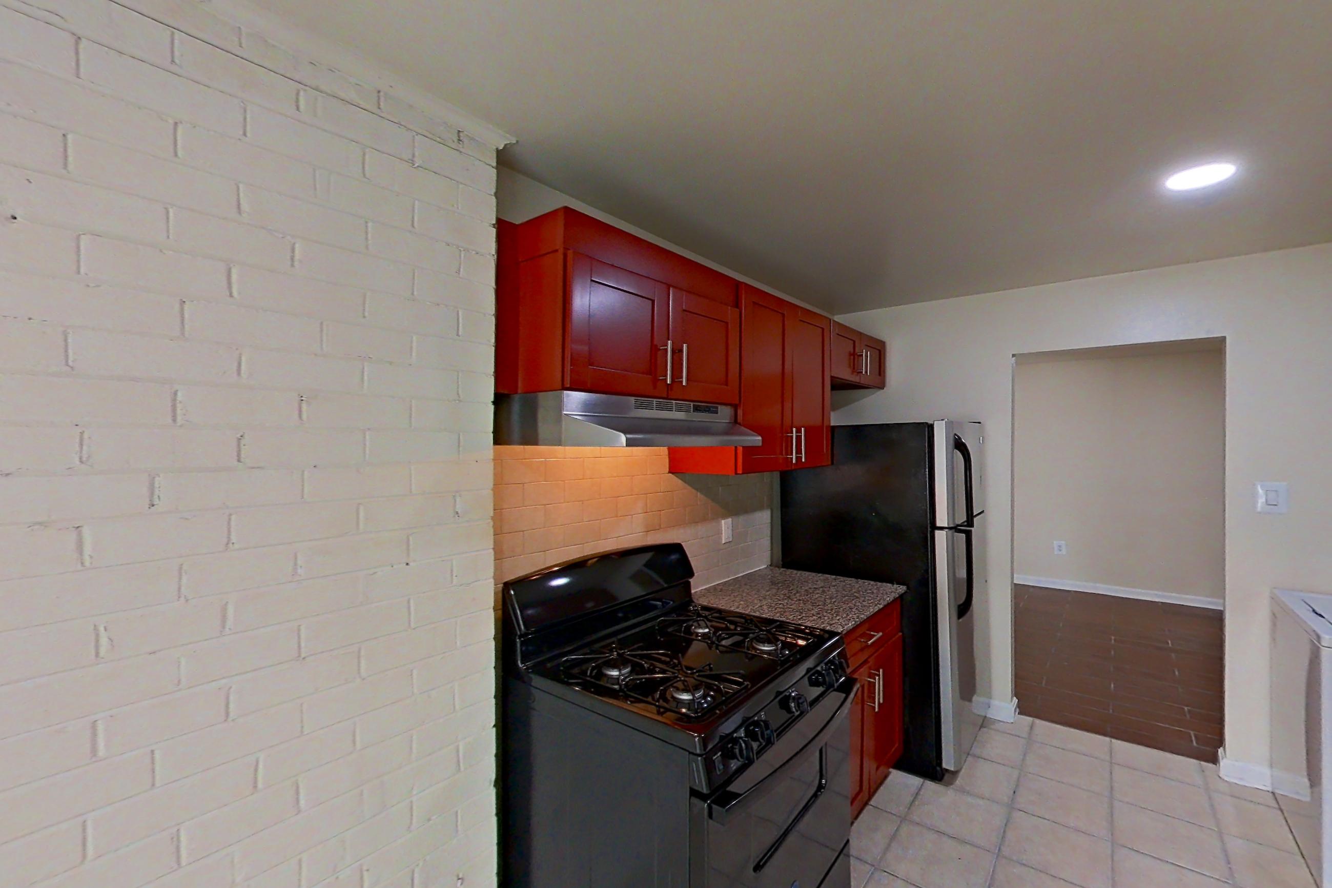 Kitchen with black appliances, dark stone countertops, dishwasher, gas range, in-unit laundry, light countertops, light tile flooring, oven/range, and range hood, Apartment 9326ER12 at Franklin Park at Greenbelt Station