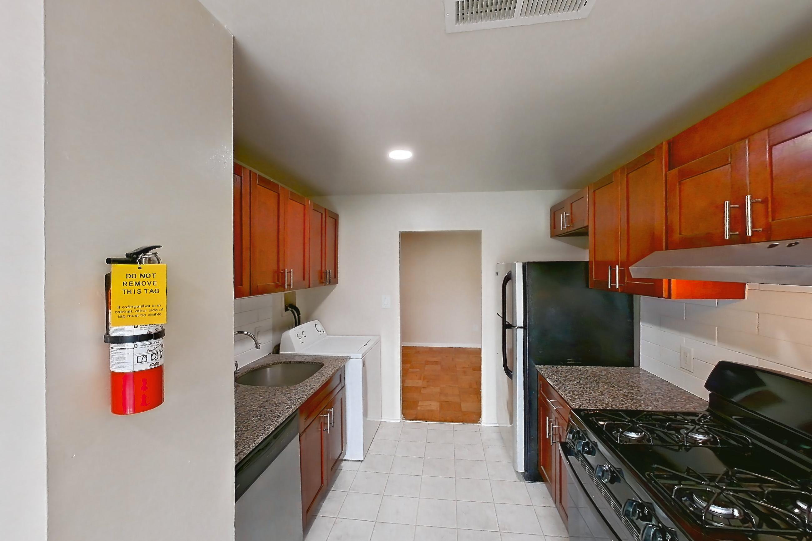 Kitchen with black appliances, dark stone countertops, dishwasher, gas range, in-unit laundry, light countertops, light tile flooring, oven/range, refrigerator, and stainless steel appliances, Apartment 9328ER31 at Franklin Park at Greenbelt Station