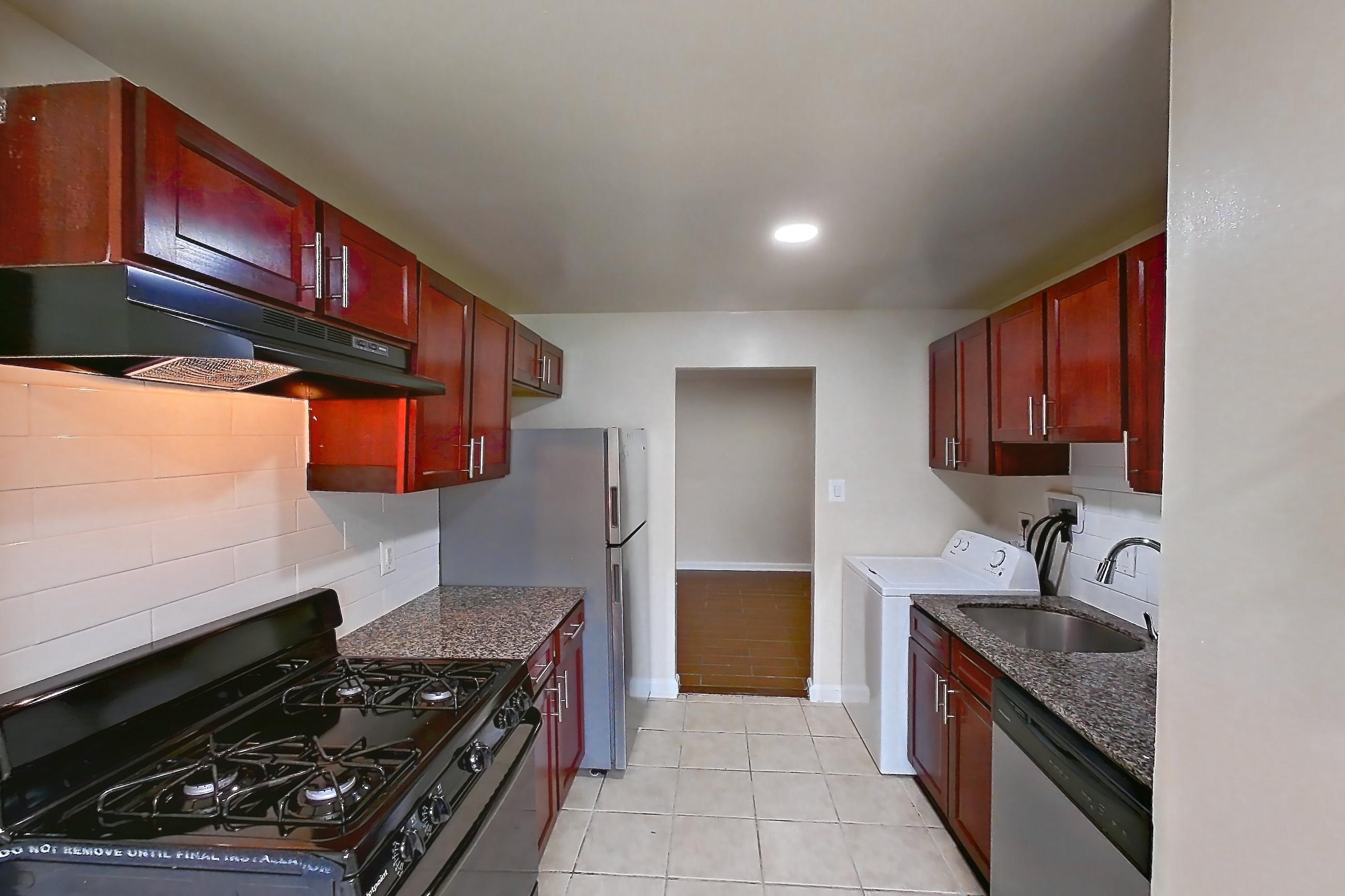 Kitchen with black appliances, dark stone countertops, dishwasher, gas range, in-unit laundry, light countertops, light tile flooring, oven/range, range hood, refrigerator, and stainless steel appliances, Apartment 9340ER14 at Franklin Park at Greenbelt Station