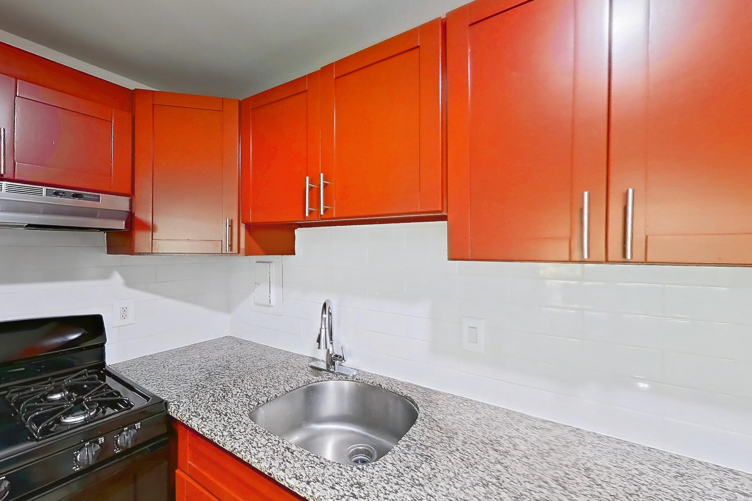 Kitchen with black appliances, dishwasher, gas range, light countertops, light stone countertops, light wood-finish flooring, oven/range, range hood, and stainless steel appliances, Apartment 5915CL14 at Franklin Park at Greenbelt Station