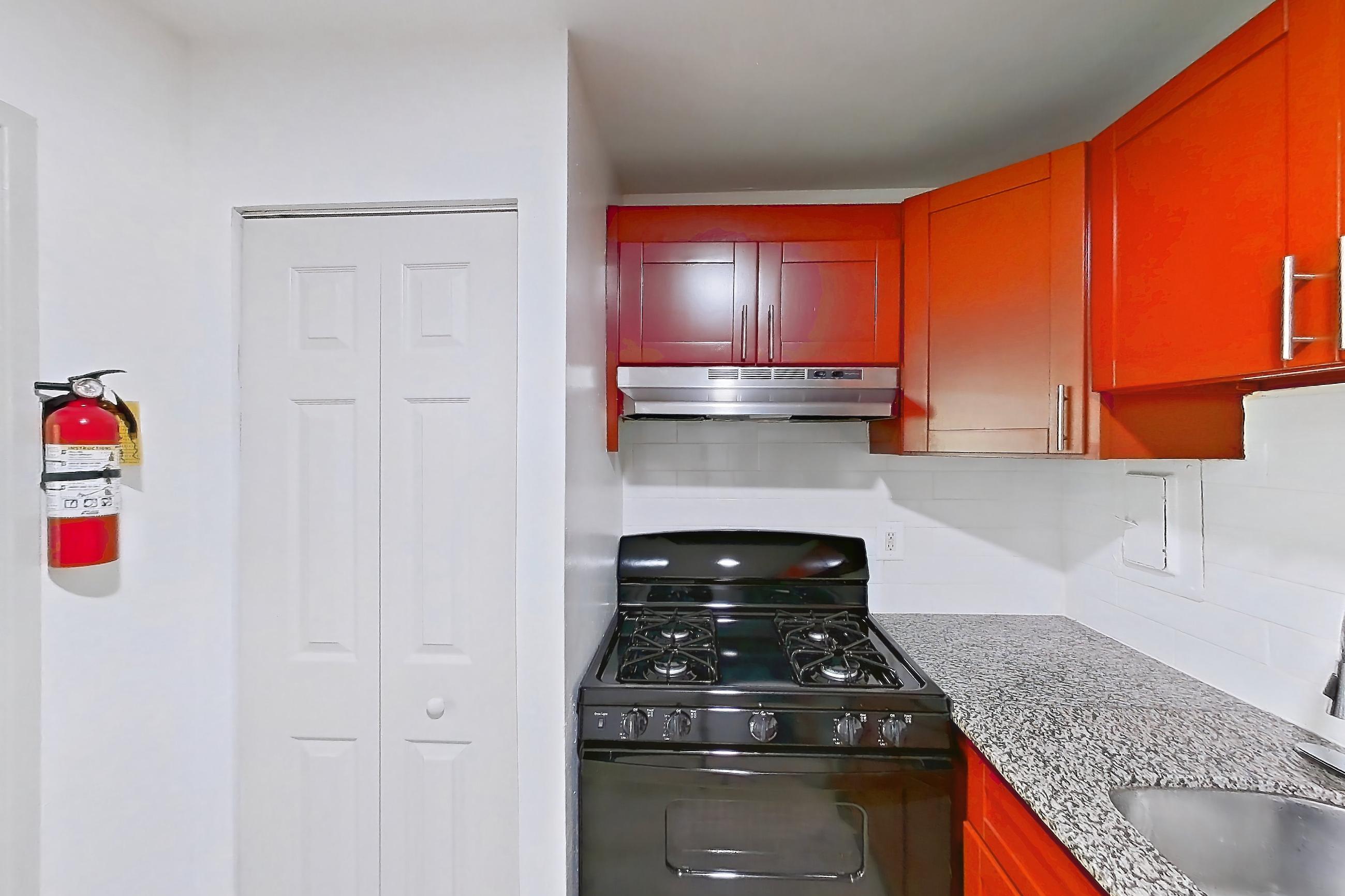 Kitchen with black appliances, dishwasher, gas range, light countertops, light stone countertops, light wood-finish flooring, oven/range, range hood, and stainless steel appliances, Apartment 5915CL14 at Franklin Park at Greenbelt Station