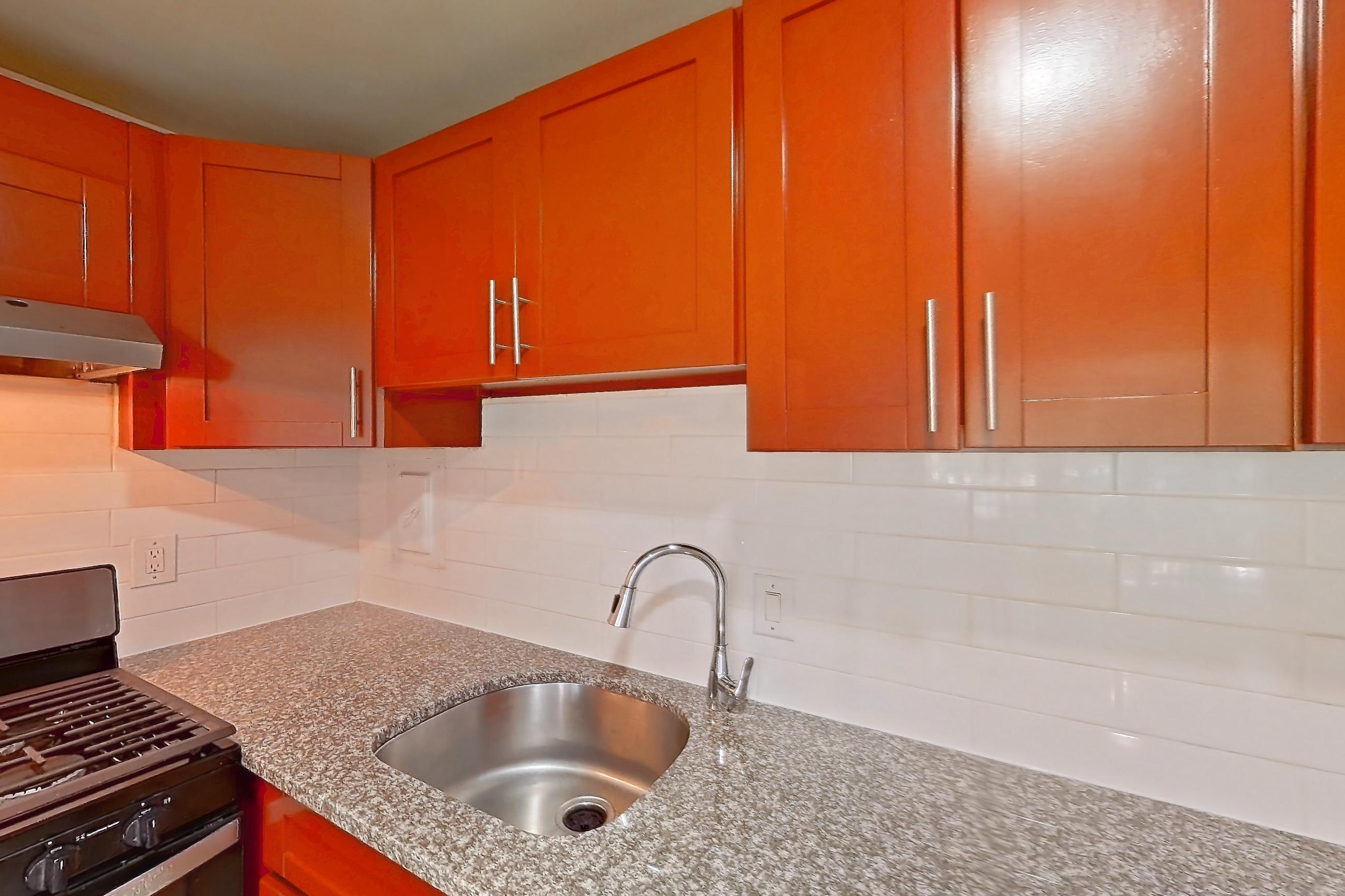 Kitchen with black appliances, dark stone countertops, dishwasher, gas range, light countertops, light stone countertops, light wood-finish flooring, oven/range, range hood, and stainless steel appliances, Apartment 5915CT31 at Franklin Park at Greenbelt Station