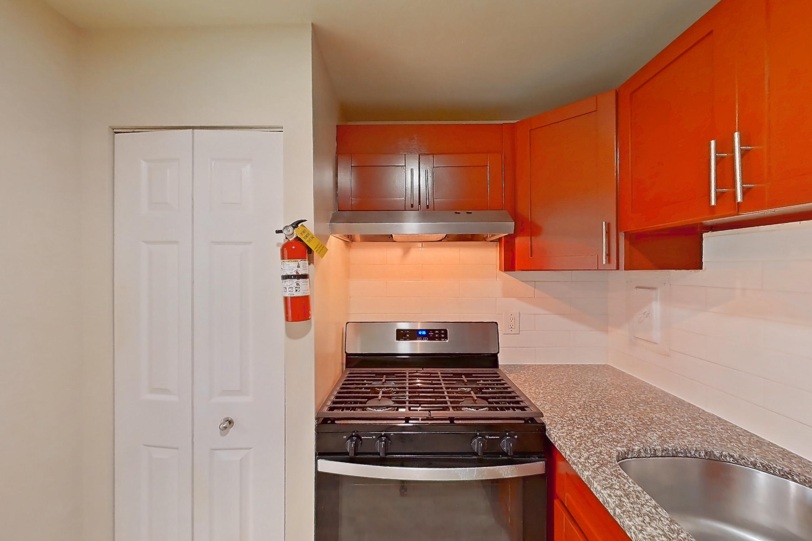 Kitchen with black appliances, dark stone countertops, dishwasher, gas range, light countertops, light stone countertops, light wood-finish flooring, oven/range, range hood, and stainless steel appliances, Apartment 5915CT31 at Franklin Park at Greenbelt Station