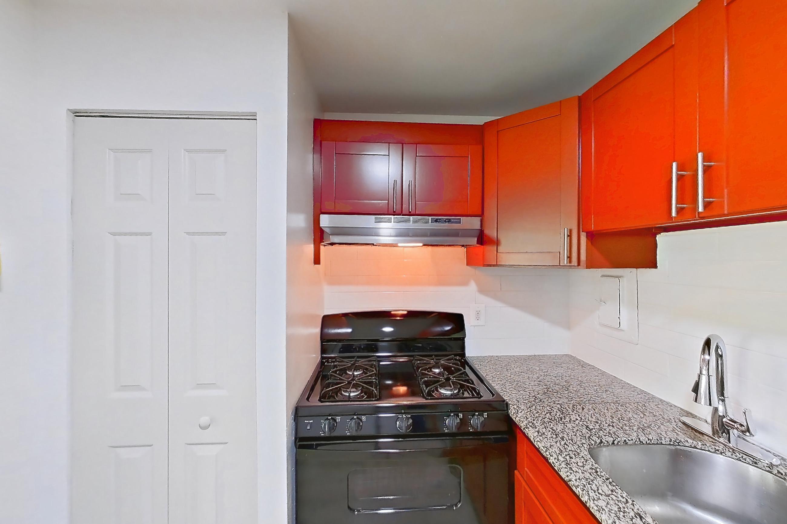 Kitchen with black appliances, dishwasher, gas range, light countertops, light stone countertops, light wood-finish flooring, oven/range, range hood, and stainless steel appliances, Apartment 5919CT34 at Franklin Park at Greenbelt Station