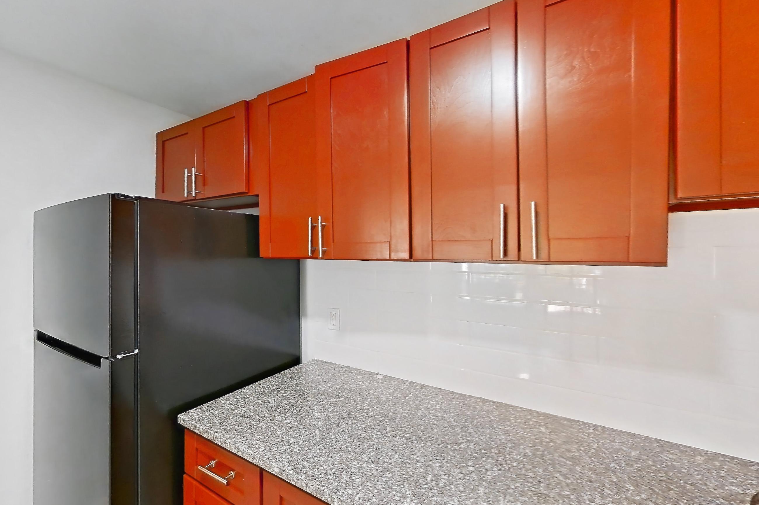 Kitchen with black appliances, dark stone countertops, dishwasher, electric range, gas range, light countertops, light wood-finish flooring, oven/range, range hood, and stainless steel appliances, Apartment 5921CT22 at Franklin Park at Greenbelt Station