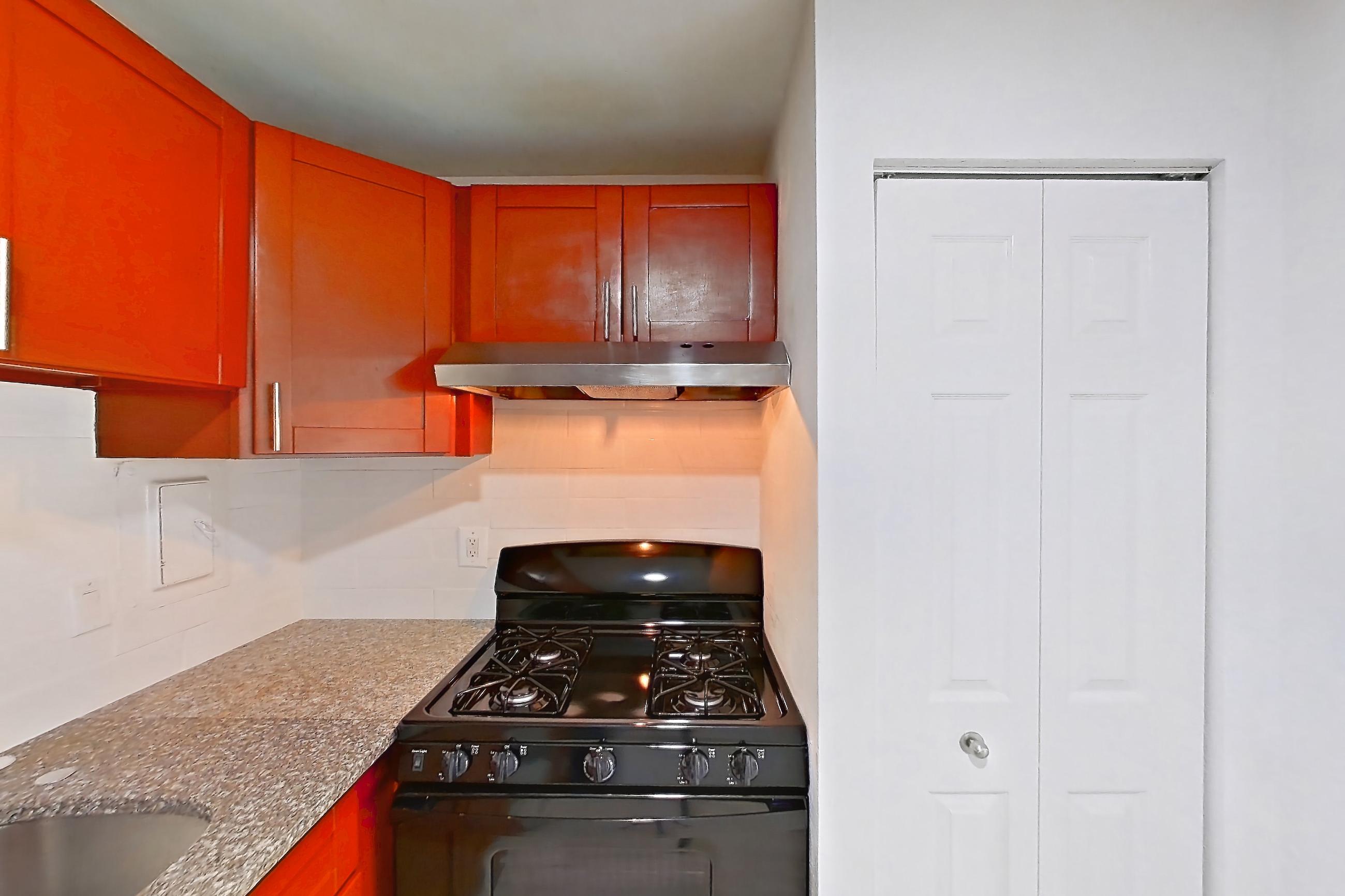 Kitchen with black appliances, dark stone countertops, dishwasher, electric range, gas range, light countertops, light wood-finish flooring, oven/range, range hood, and stainless steel appliances, Apartment 5921CT22 at Franklin Park at Greenbelt Station