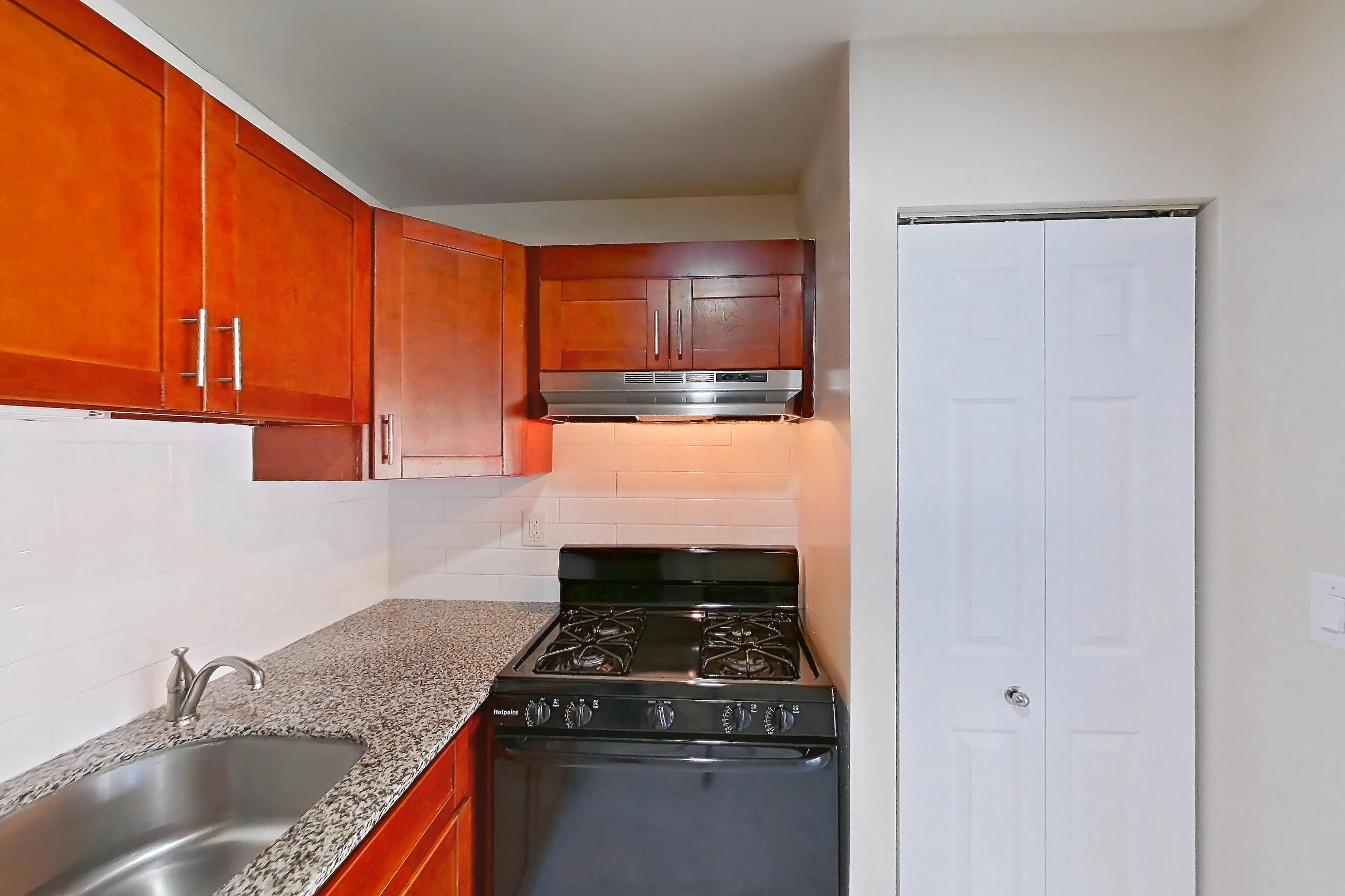Kitchen with black appliances, dishwasher, gas range, light countertops, light stone countertops, light tile flooring, oven/range, range hood, and stainless steel appliances, Apartment 5925CT32 at Franklin Park at Greenbelt Station