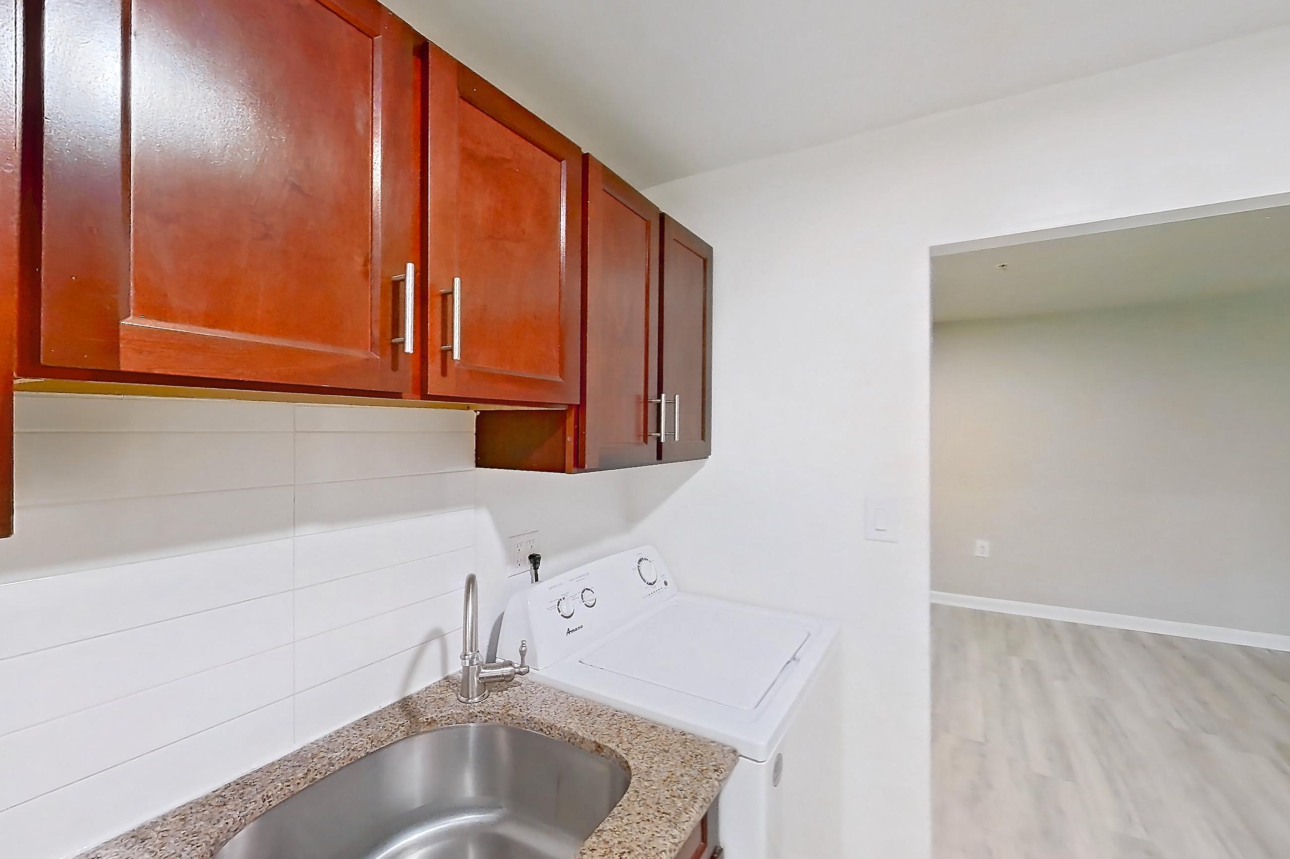 Kitchen with black appliances, gas range, in-unit laundry, light countertops, light stone countertops, light wood-finish flooring, oven/range, range hood, refrigerator, stainless steel appliances, and white appliances, Apartment 9010BT31 at Franklin Park at Greenbelt Station