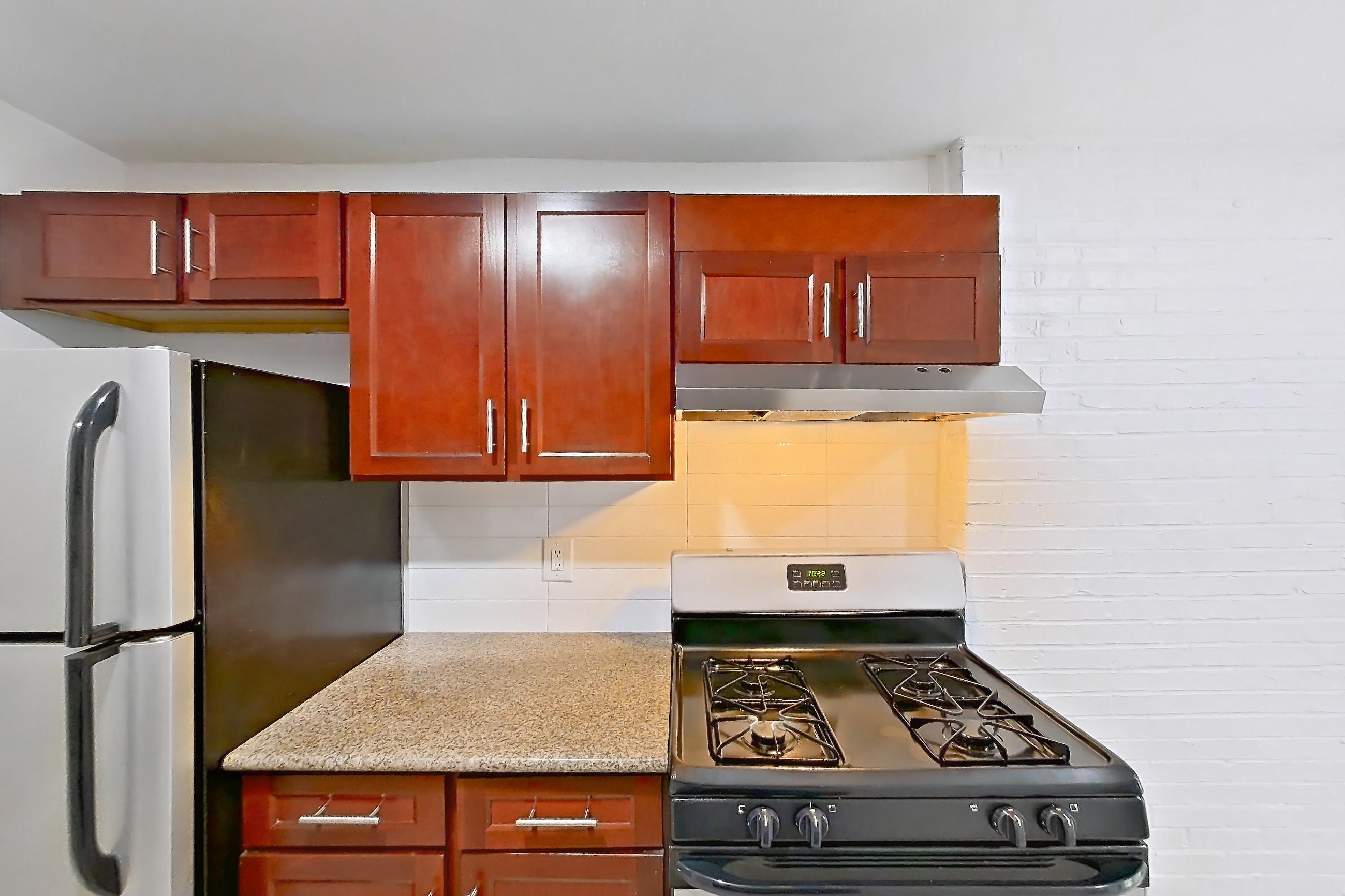Kitchen with black appliances, gas range, in-unit laundry, light countertops, light stone countertops, light wood-finish flooring, oven/range, range hood, refrigerator, stainless steel appliances, and white appliances, Apartment 9010BT31 at Franklin Park at Greenbelt Station