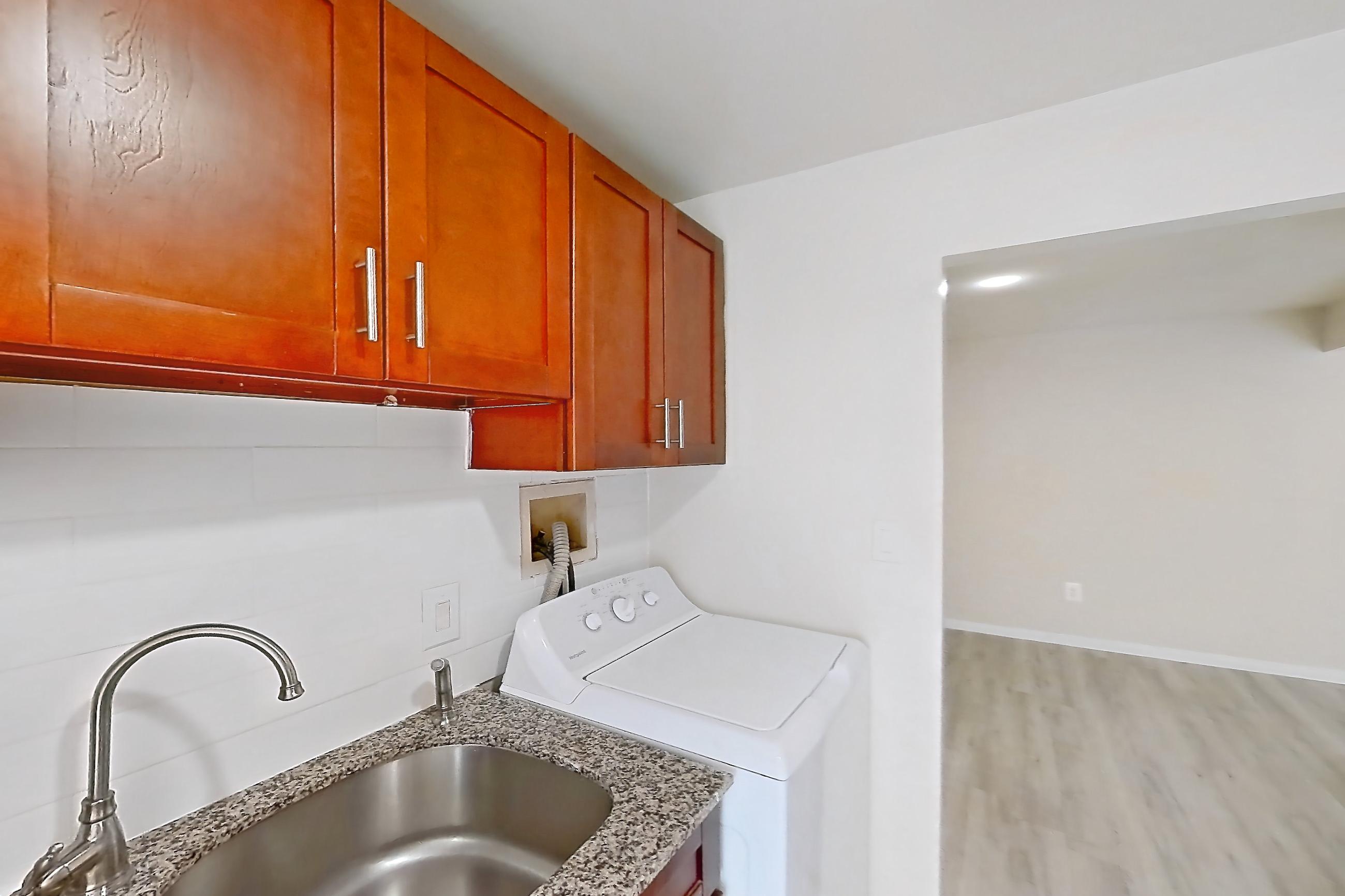 Kitchen with black appliances, gas range, in-unit laundry, light countertops, light stone countertops, light wood-finish flooring, oven/range, range hood, refrigerator, and stainless steel appliances, Apartment 9011BT21 at Franklin Park at Greenbelt Station