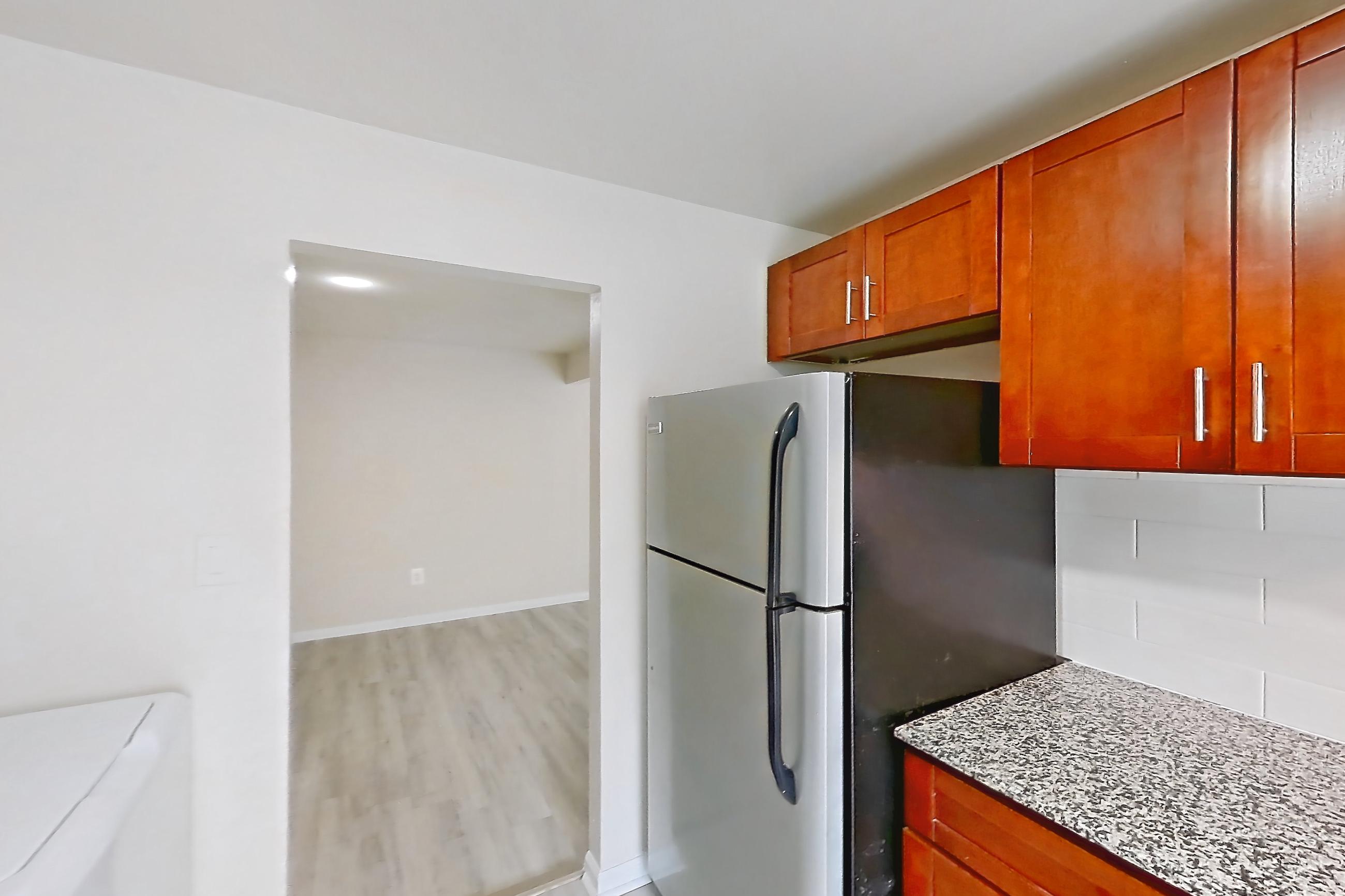 Kitchen with black appliances, gas range, in-unit laundry, light countertops, light stone countertops, light wood-finish flooring, oven/range, range hood, refrigerator, and stainless steel appliances, Apartment 9011BT21 at Franklin Park at Greenbelt Station