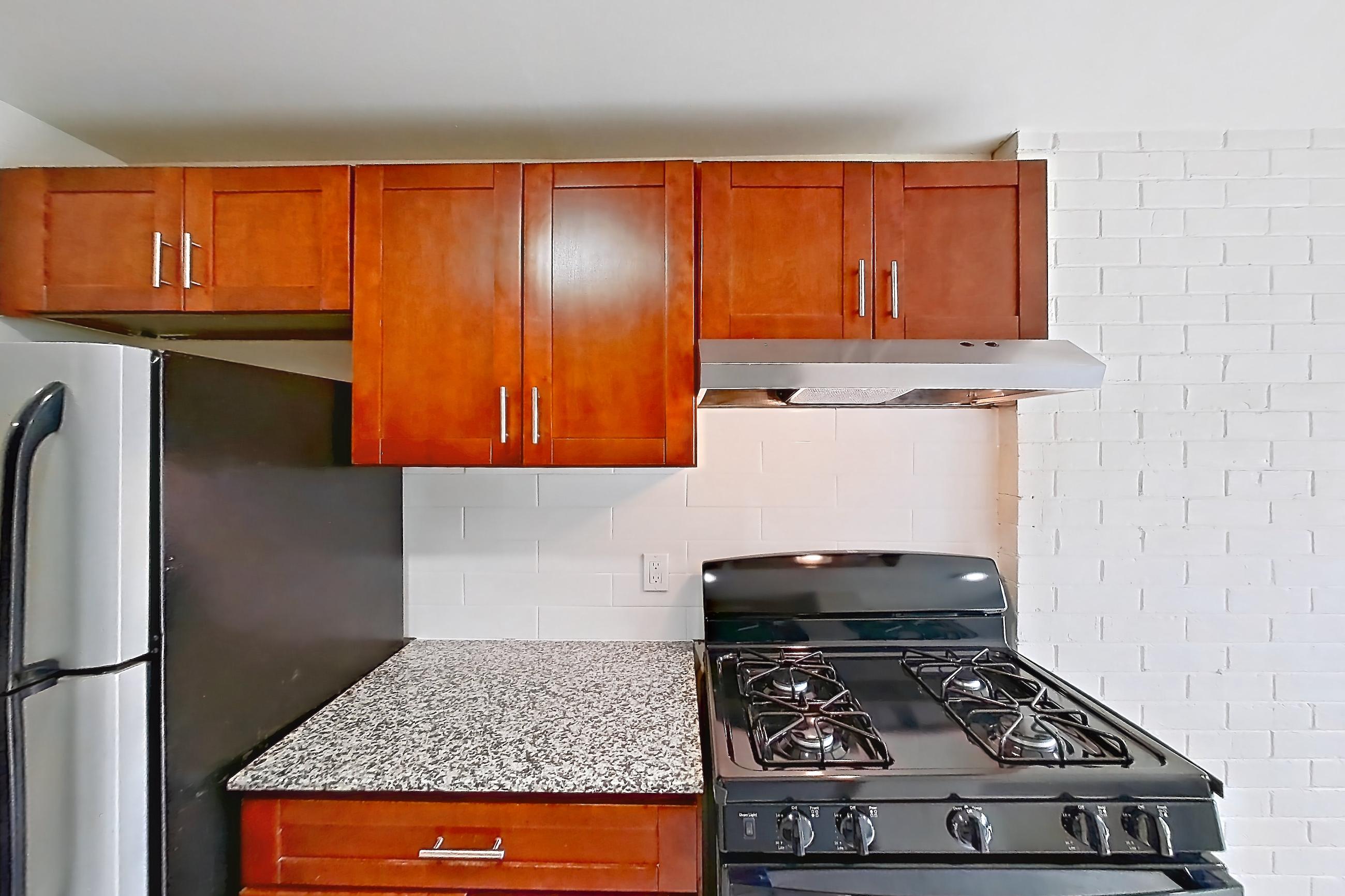 Kitchen with black appliances, gas range, in-unit laundry, light countertops, light stone countertops, light wood-finish flooring, oven/range, range hood, refrigerator, and stainless steel appliances, Apartment 9011BT21 at Franklin Park at Greenbelt Station