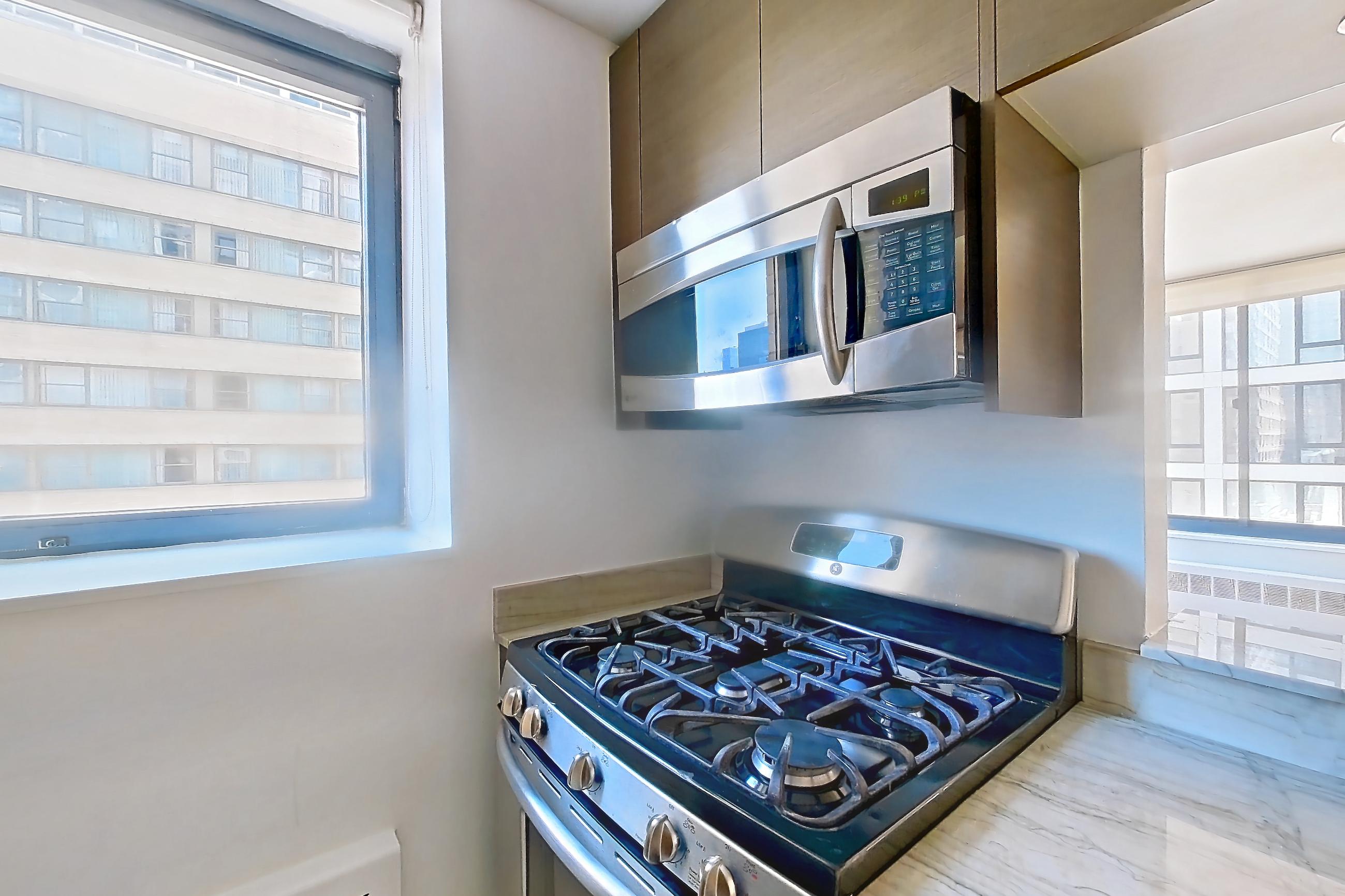 Kitchen with dishwasher, gas range, light countertops, light stone countertops, light tile flooring, microwave, oven/range, and stainless steel appliances, Apartment 10M at Stonehenge Leasing