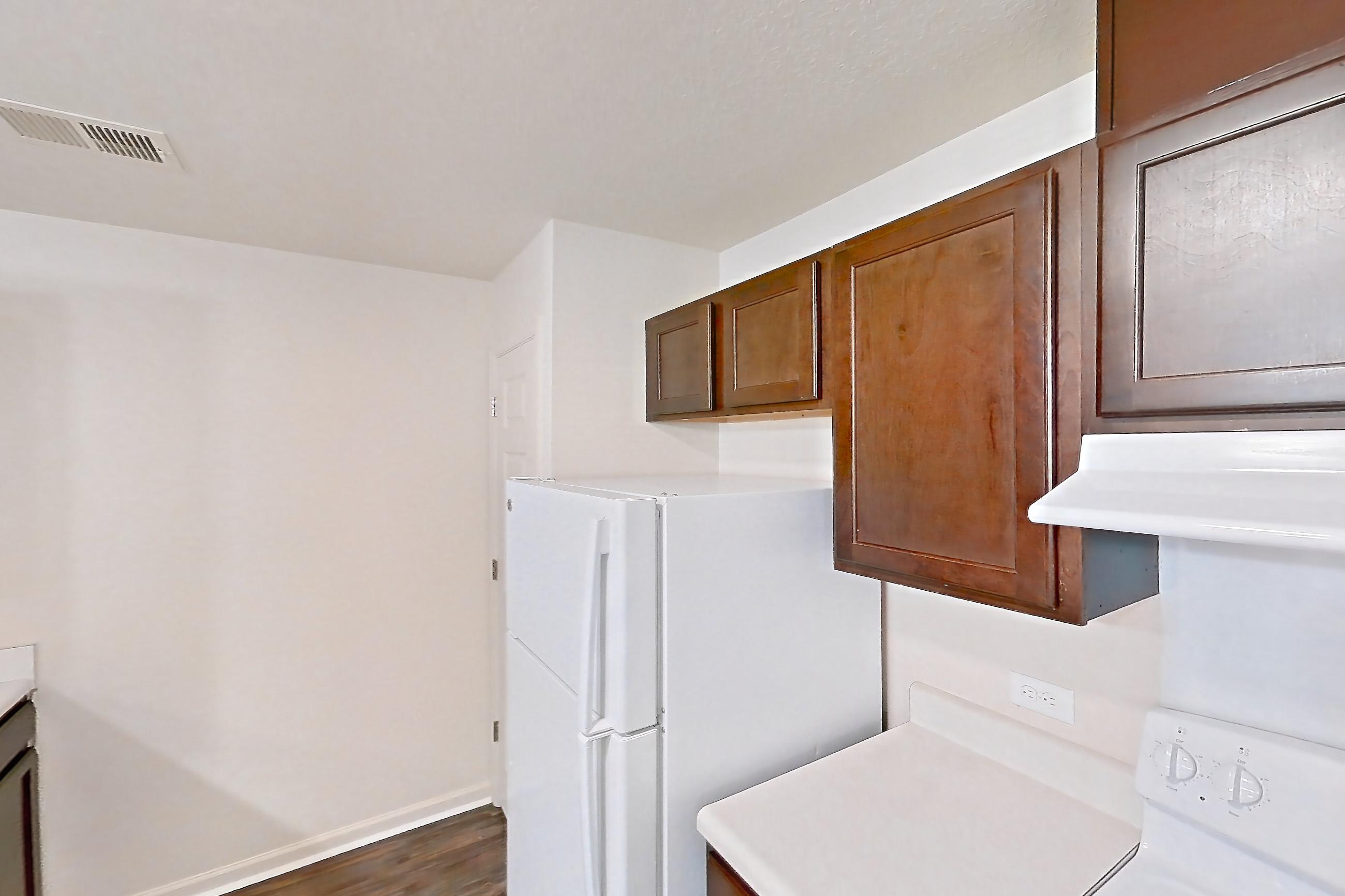 Kitchen with dark wood-finish flooring, dishwasher, electric range, light countertops, oven/range, range hood, refrigerator, and white appliances, Apartment 6481-104 at Ashley Estates