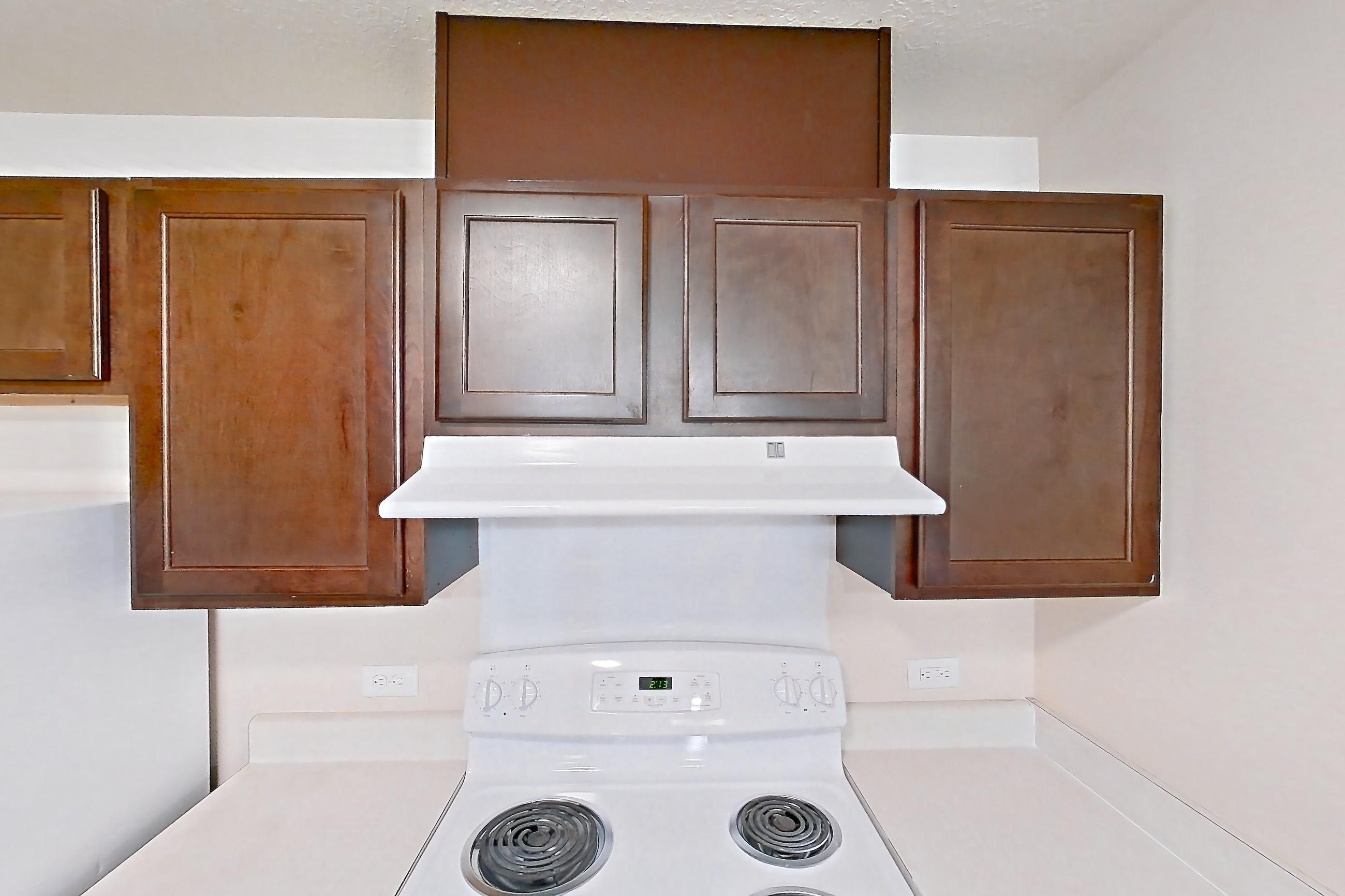 Kitchen with dark wood-finish flooring, dishwasher, electric range, light countertops, oven/range, range hood, refrigerator, and white appliances, Apartment 6481-104 at Ashley Estates