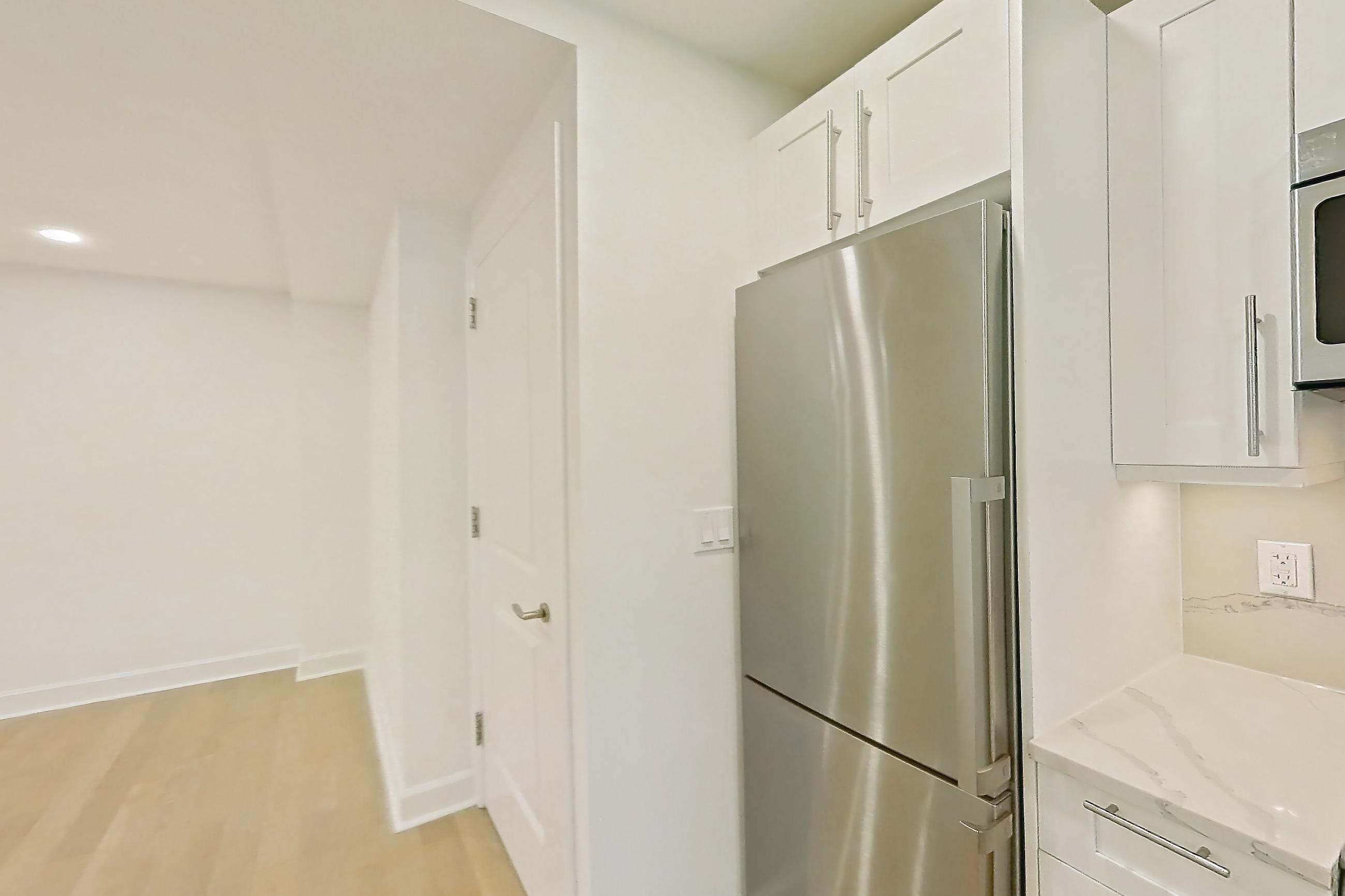 Kitchen with electric range, light countertops, light stone countertops, light wood-finish flooring, microwave, oven/range, refrigerator, and stainless steel appliances, Apartment 10K at The Buchanan