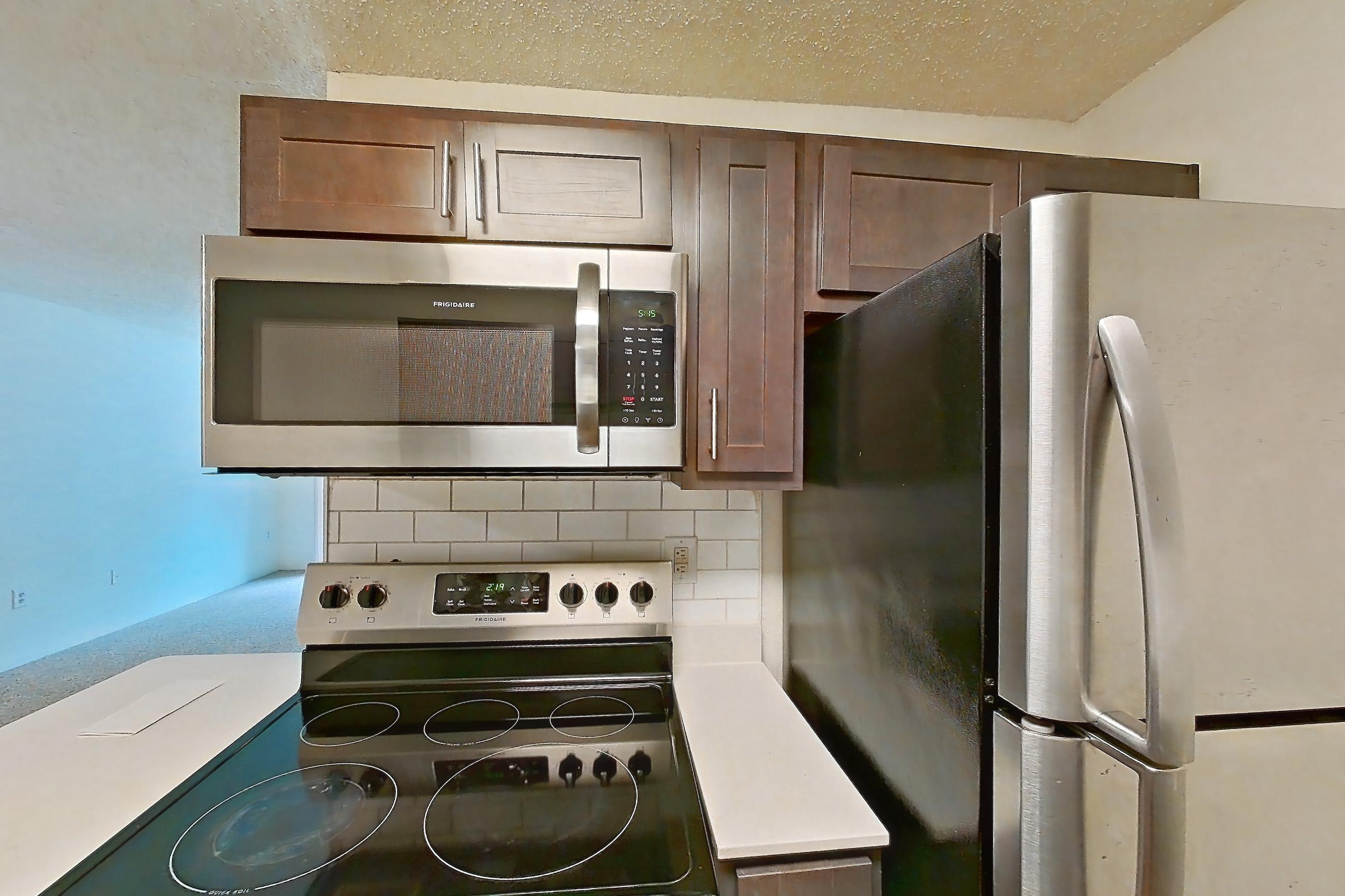 Kitchen with electric range, light countertops, light wood-finish flooring, microwave, oven/range, refrigerator, stainless steel appliances, and white appliances, Apartment 61302 at The Boulders