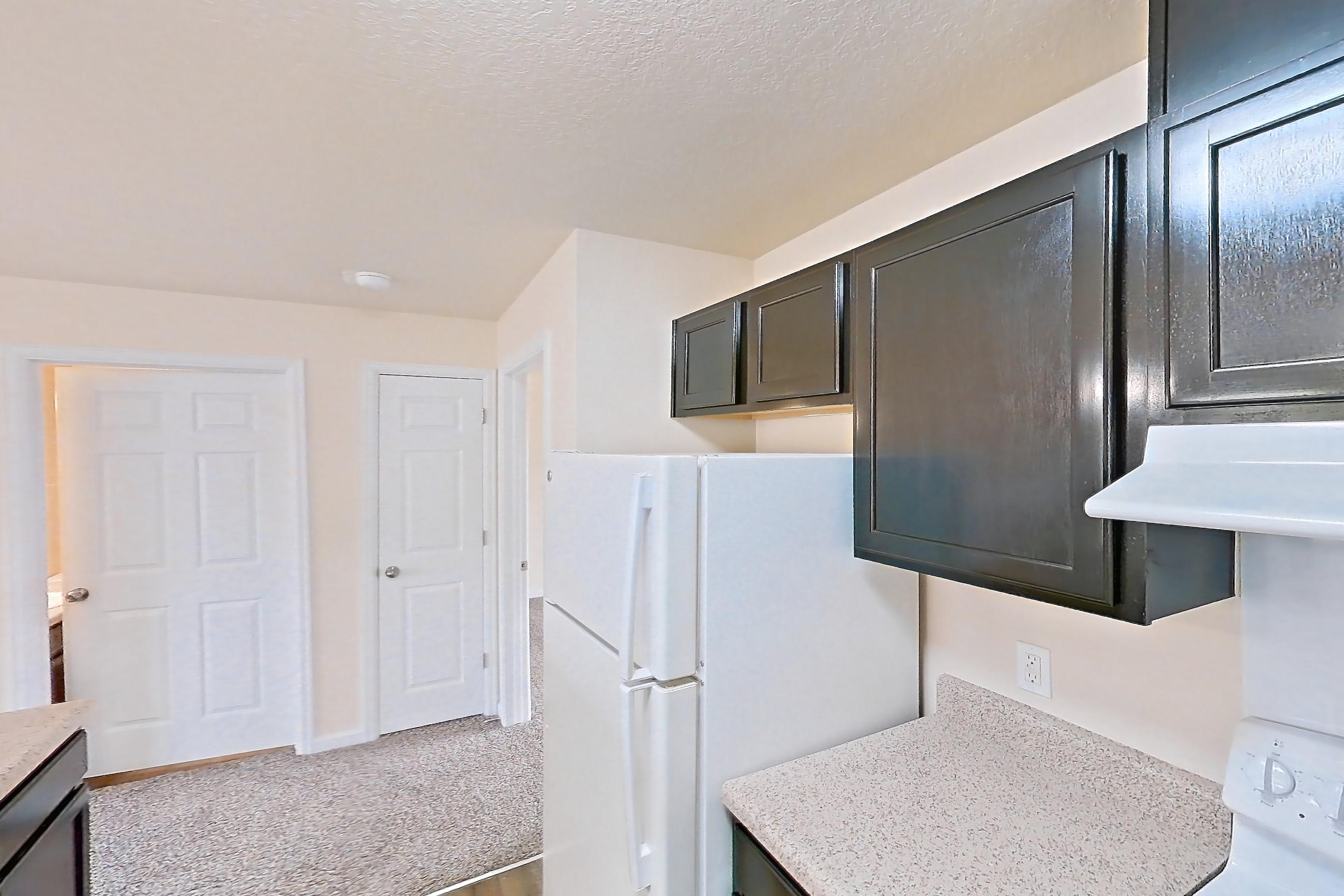 Kitchen with dark wood-finish flooring, dishwasher, electric range, light countertops, light stone countertops, oven/range, refrigerator, and white appliances, Apartment 19453 E 57th Ave - Unit 202 at The Meadows at Dunkirk