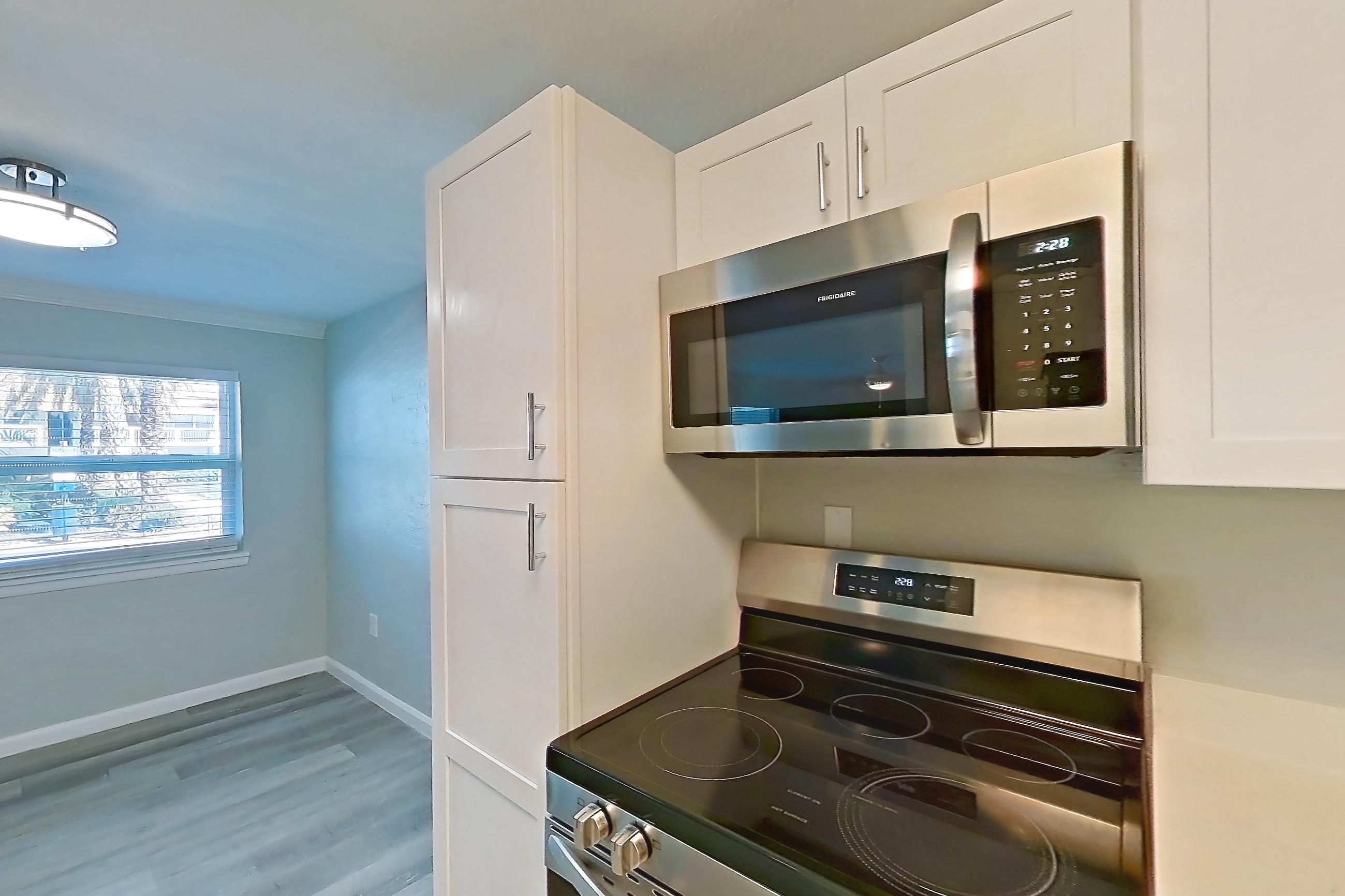 Kitchen with dishwasher, electric range, light countertops, light stone countertops, light wood-finish flooring, microwave, oven/range, refrigerator, and stainless steel appliances, Apartment 21 at Riverwalk Apartments