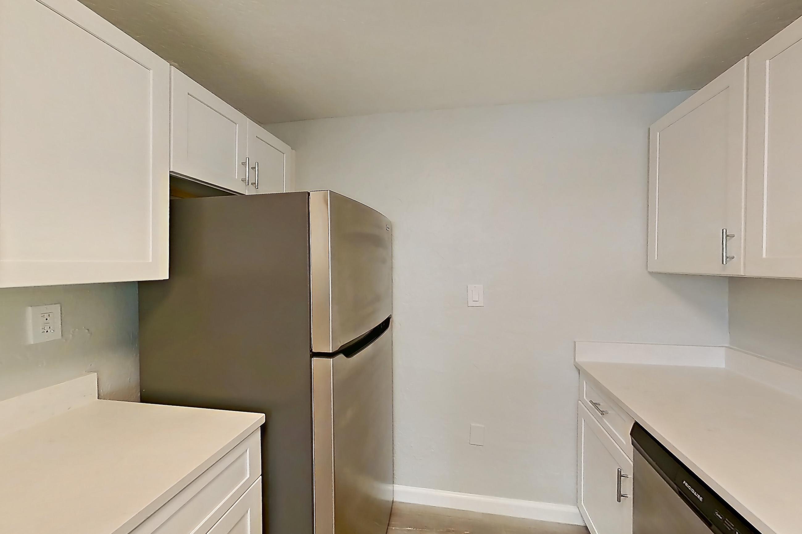 Kitchen with dishwasher, electric range, light countertops, light stone countertops, light wood-finish flooring, microwave, oven/range, refrigerator, and stainless steel appliances, Apartment 21 at Riverwalk Apartments