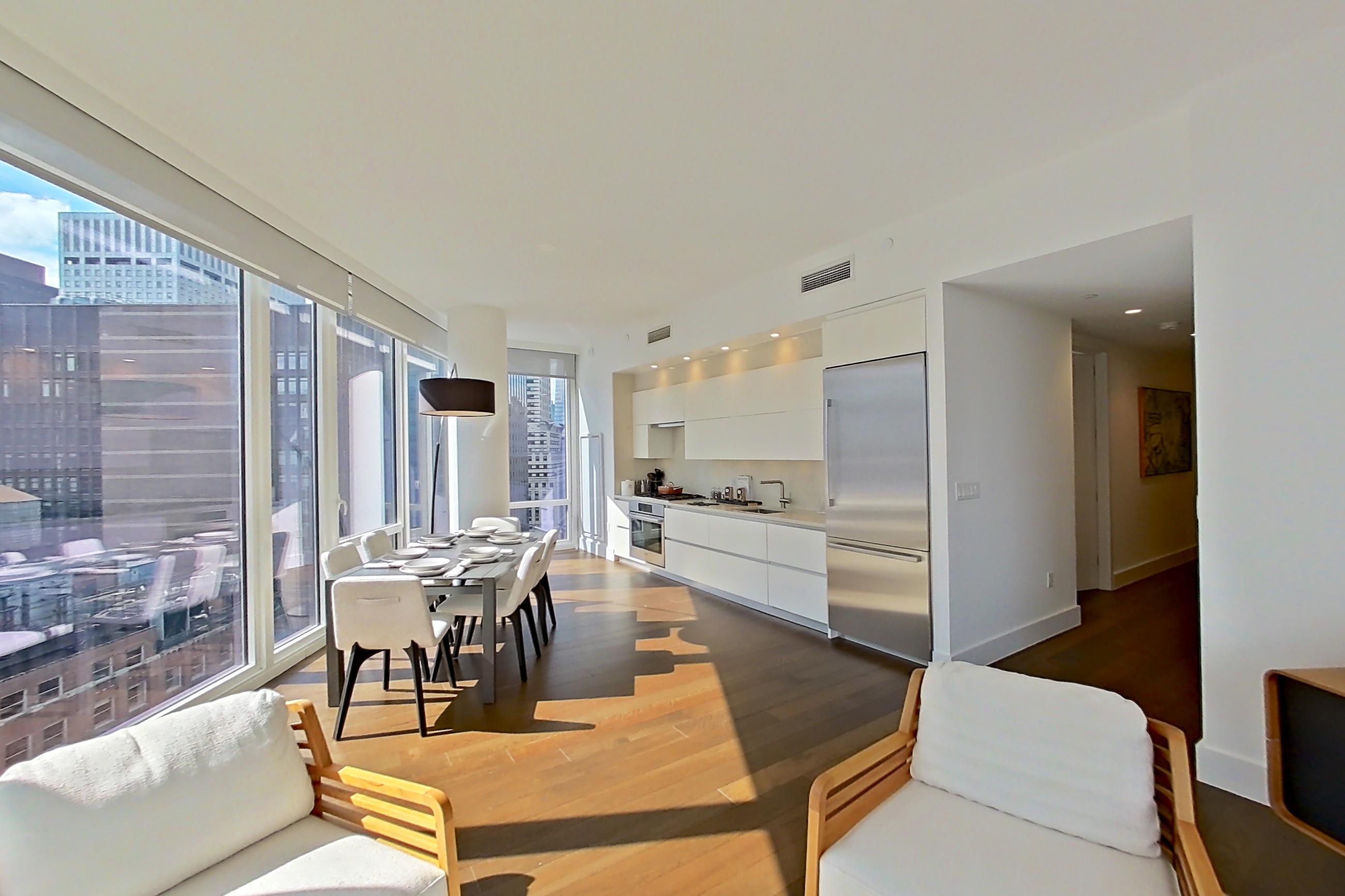 Living room with city view, dark wood-finish flooring, oven/range, refrigerator, skyline view, and stainless steel appliances, Apartment 28E at Summit NYC