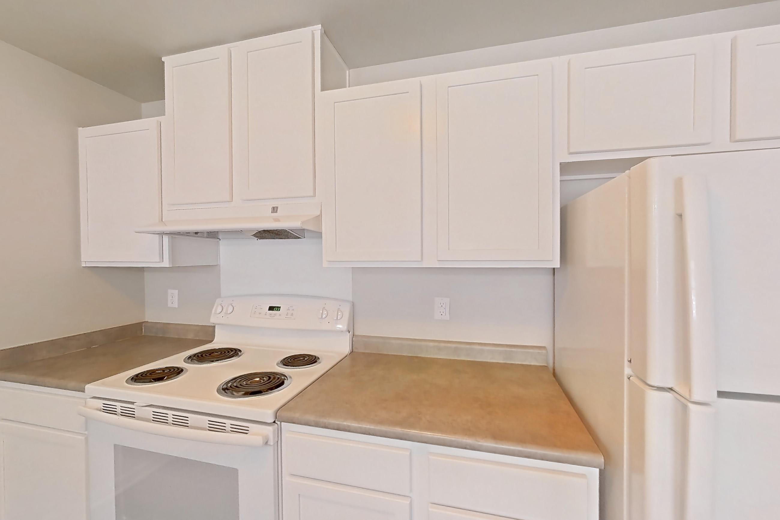 Kitchen with dark wood-finish flooring, dishwasher, electric range, light countertops, oven/range, range hood, refrigerator, and white appliances, Apartment 522 at Sunset View