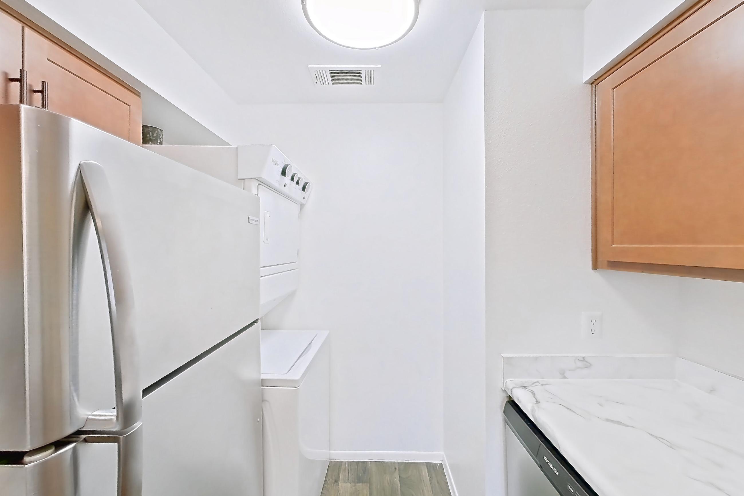 Kitchen with dark wood-finish flooring, dishwasher, electric range, light countertops, light stone countertops, light wood-finish flooring, oven/range, range hood, refrigerator, stainless steel appliances, and white appliances, Apartment 4060 Unit 10 at Aaron Lake Apartments