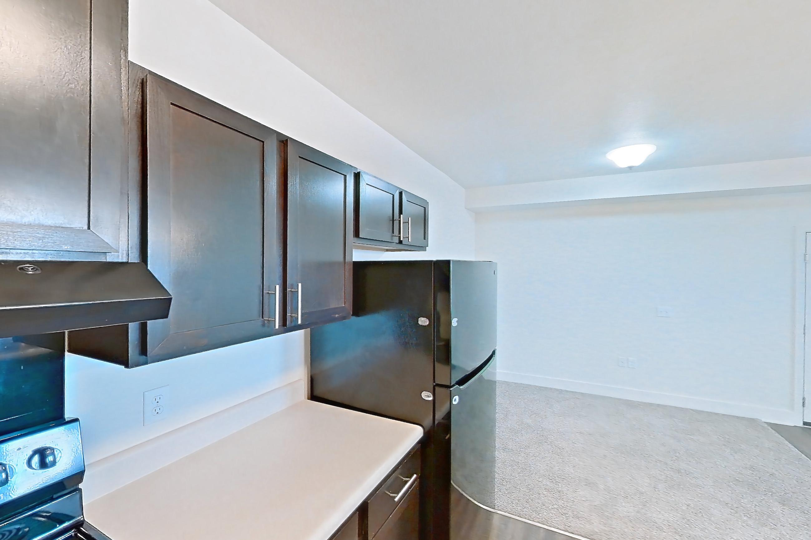 Kitchen with black appliances, dark wood-finish flooring, dishwasher, electric range, light countertops, light wood-finish flooring, oven/range, range hood, and refrigerator, Apartment 8304 at Larkridge