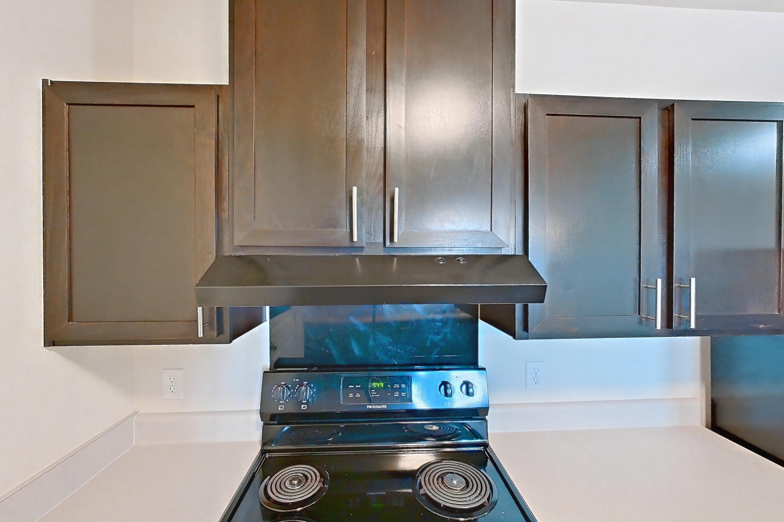 Kitchen with black appliances, dark wood-finish flooring, dishwasher, electric range, light countertops, light wood-finish flooring, oven/range, range hood, and refrigerator, Apartment 8304 at Larkridge