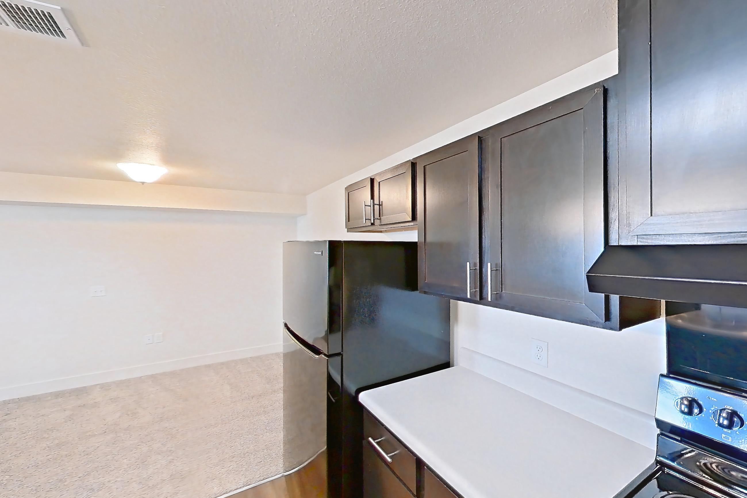 Kitchen with black appliances, dark wood-finish flooring, dishwasher, electric range, light countertops, oven/range, range hood, refrigerator, and stainless steel appliances, Apartment 4205 at Larkridge