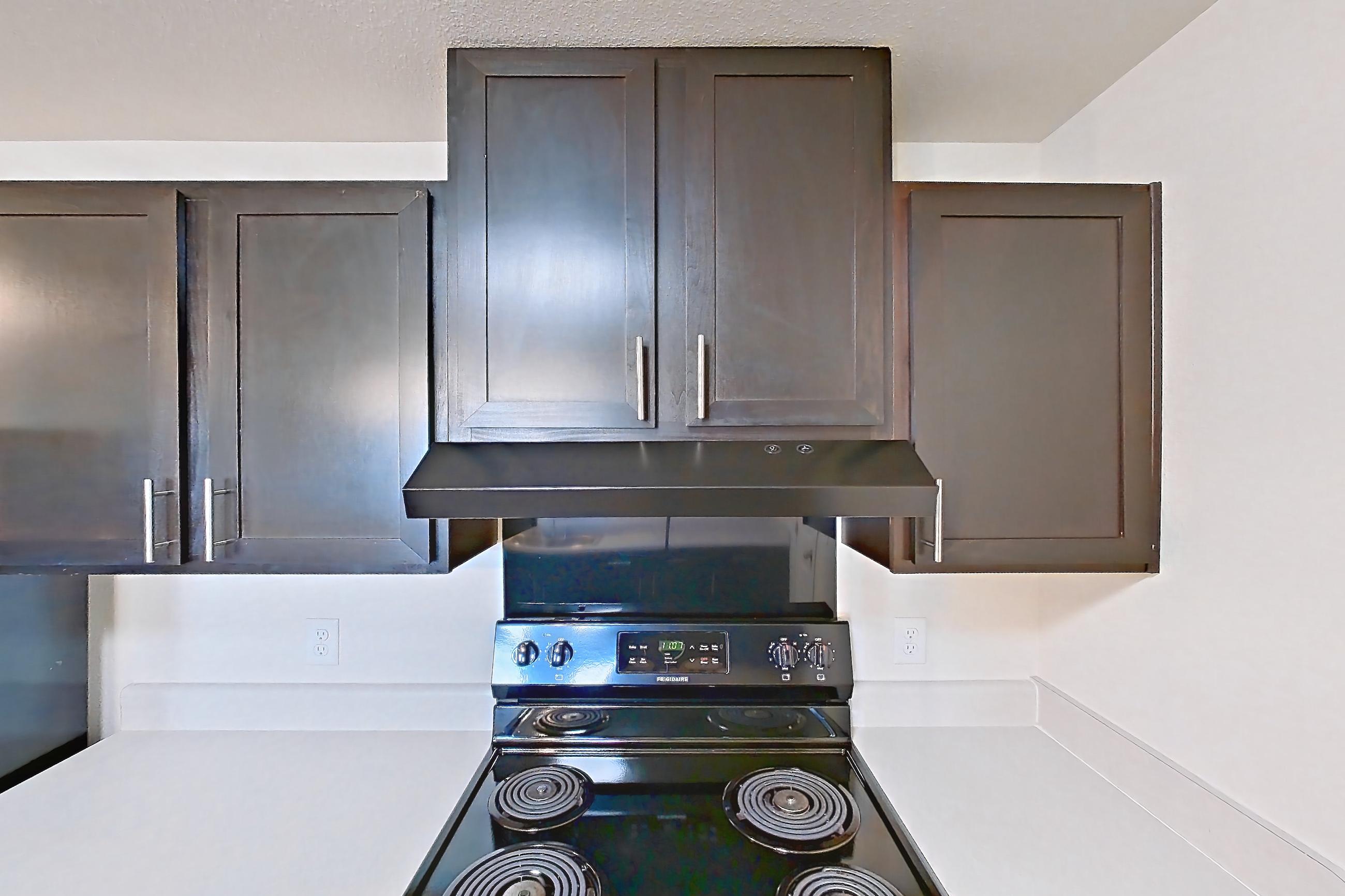 Kitchen with black appliances, dark wood-finish flooring, dishwasher, electric range, light countertops, oven/range, range hood, refrigerator, and stainless steel appliances, Apartment 4205 at Larkridge