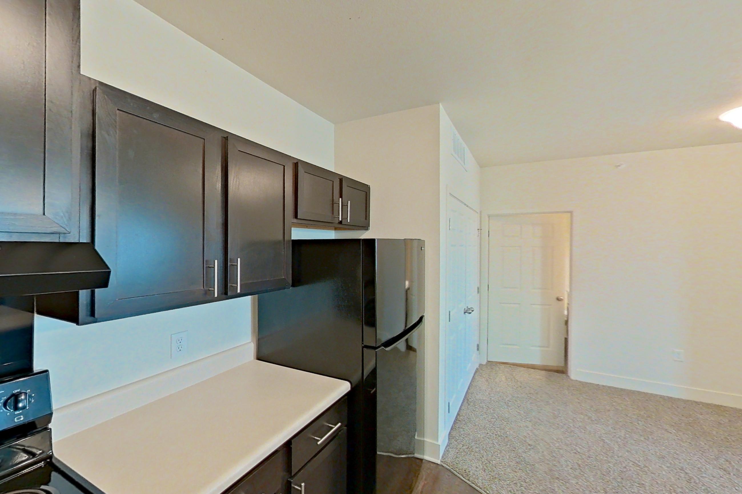 Kitchen with black appliances, dark wood-finish flooring, dishwasher, electric range, light countertops, oven/range, refrigerator, and stainless steel appliances, Apartment 4307 at Larkridge