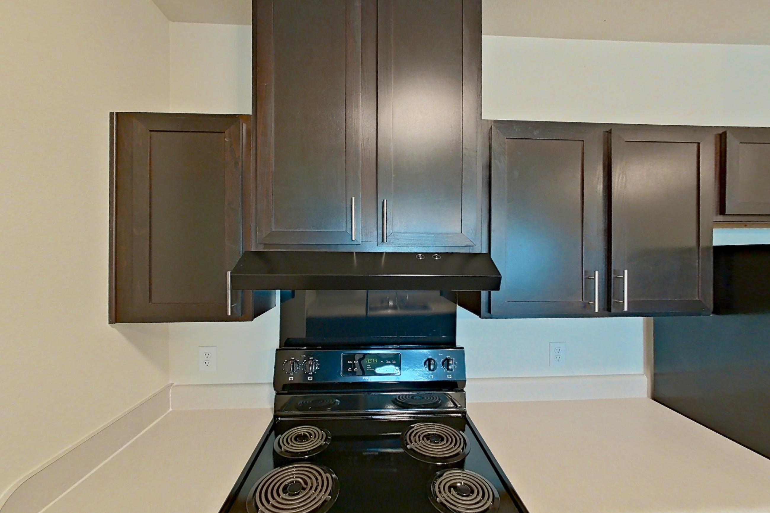 Kitchen with black appliances, dark wood-finish flooring, dishwasher, electric range, light countertops, oven/range, refrigerator, and stainless steel appliances, Apartment 4307 at Larkridge