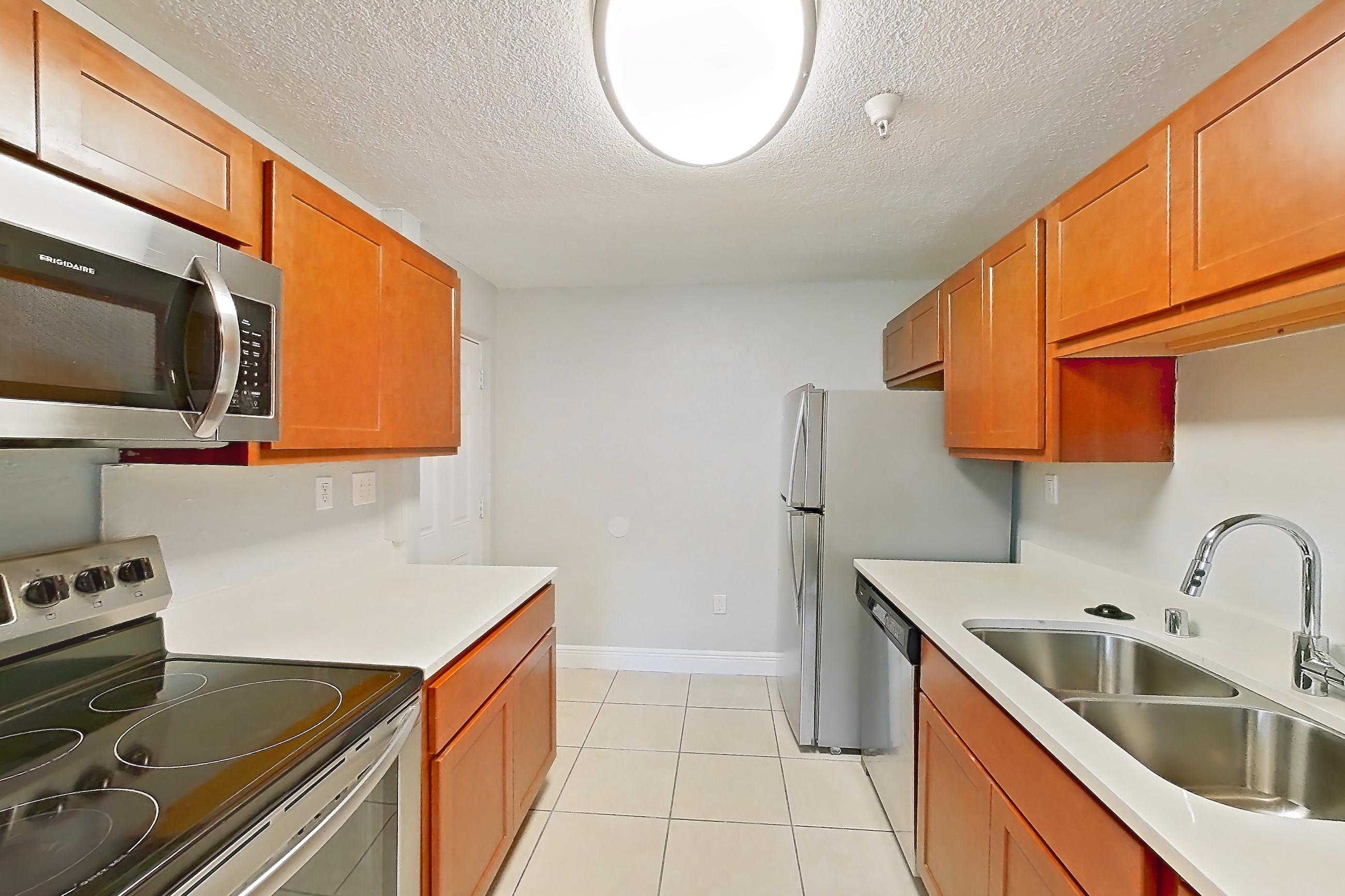 Kitchen with dishwasher, electric range, light countertops, light tile flooring, oven/range, refrigerator, stainless steel appliances, and white appliances, Apartment 46 at Riverwalk Apartments