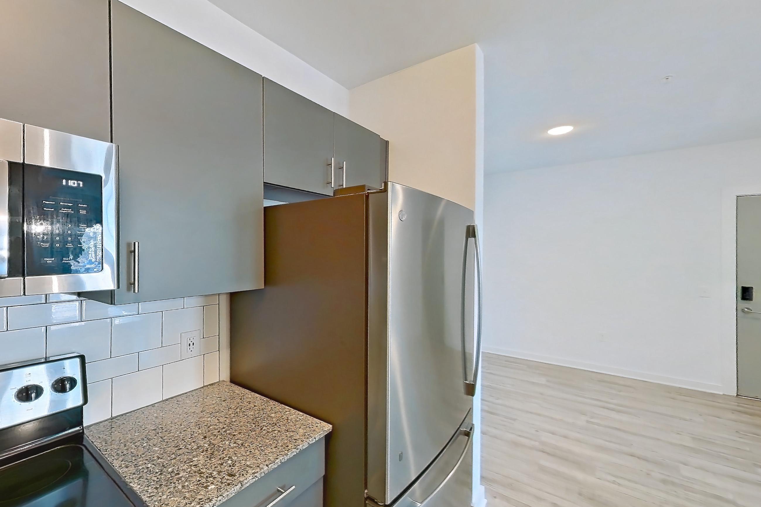 Kitchen with dark stone countertops, dishwasher, electric range, light stone countertops, light wood-finish flooring, microwave, oven/range, refrigerator, and stainless steel appliances, Apartment 1211-105 at Avril Cambridge Village