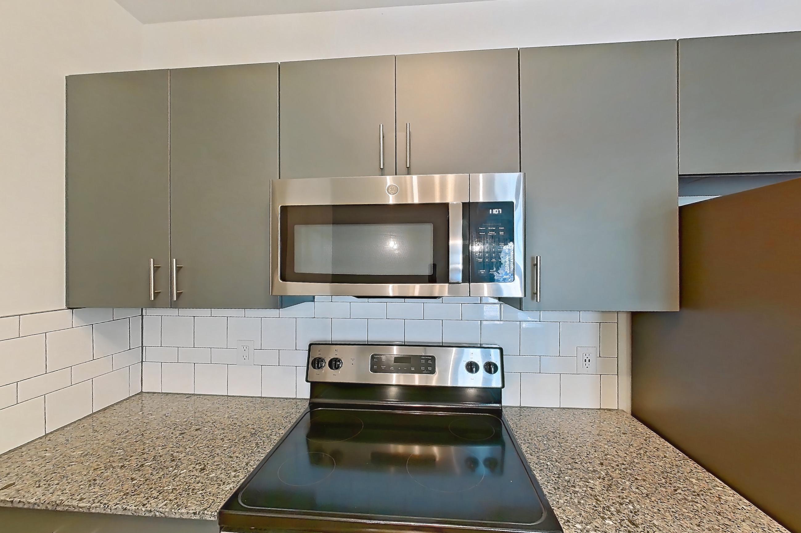 Kitchen with dark stone countertops, dishwasher, electric range, light stone countertops, light wood-finish flooring, microwave, oven/range, refrigerator, and stainless steel appliances, Apartment 1211-105 at Avril Cambridge Village