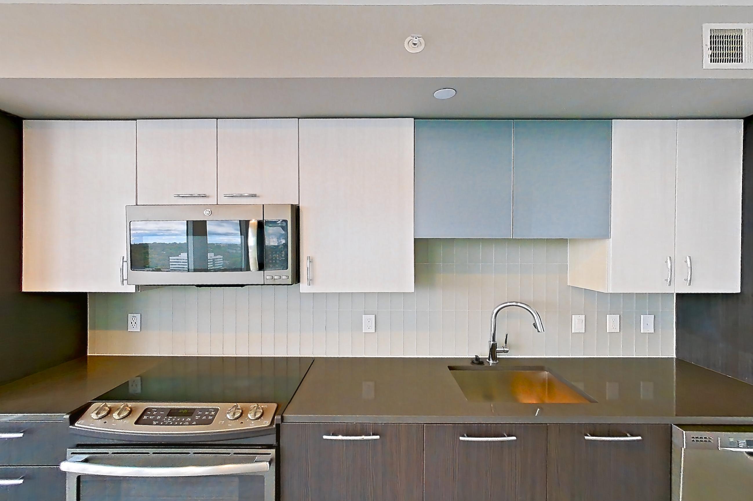 Kitchen with dark countertops, dishwasher, electric range, light wood-finish flooring, microwave, oven/range, refrigerator, and stainless steel appliances, Apartment 1811 at Adaire